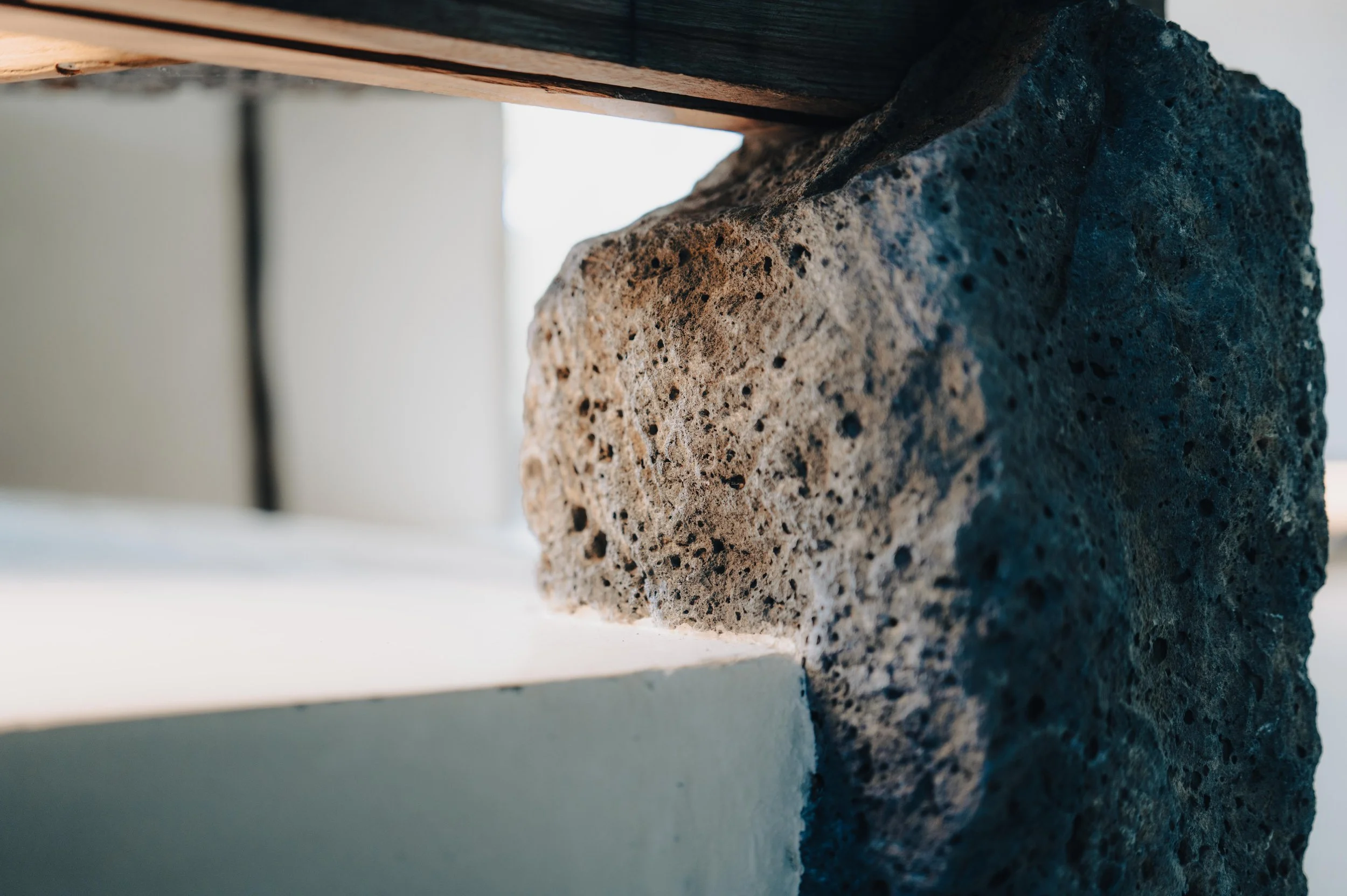 NUUT Aewol 눗애월 Close-up of a rough-textured, porous rock used as a fireplace mantle.