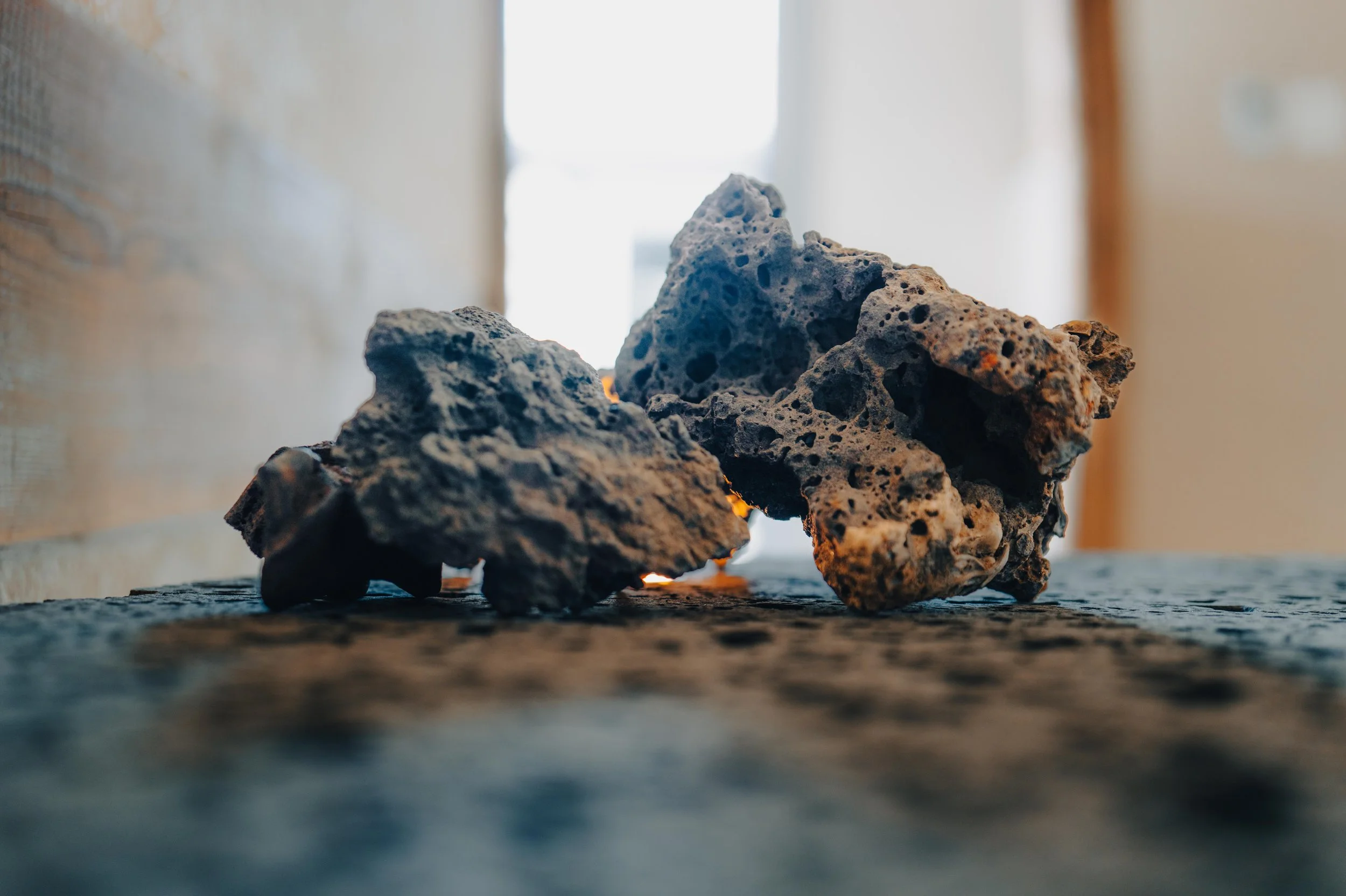 NUUT Aewol 눗애월 Close-up of irregular volcanic rocks or lava stones on a textured surface with a blurred background.