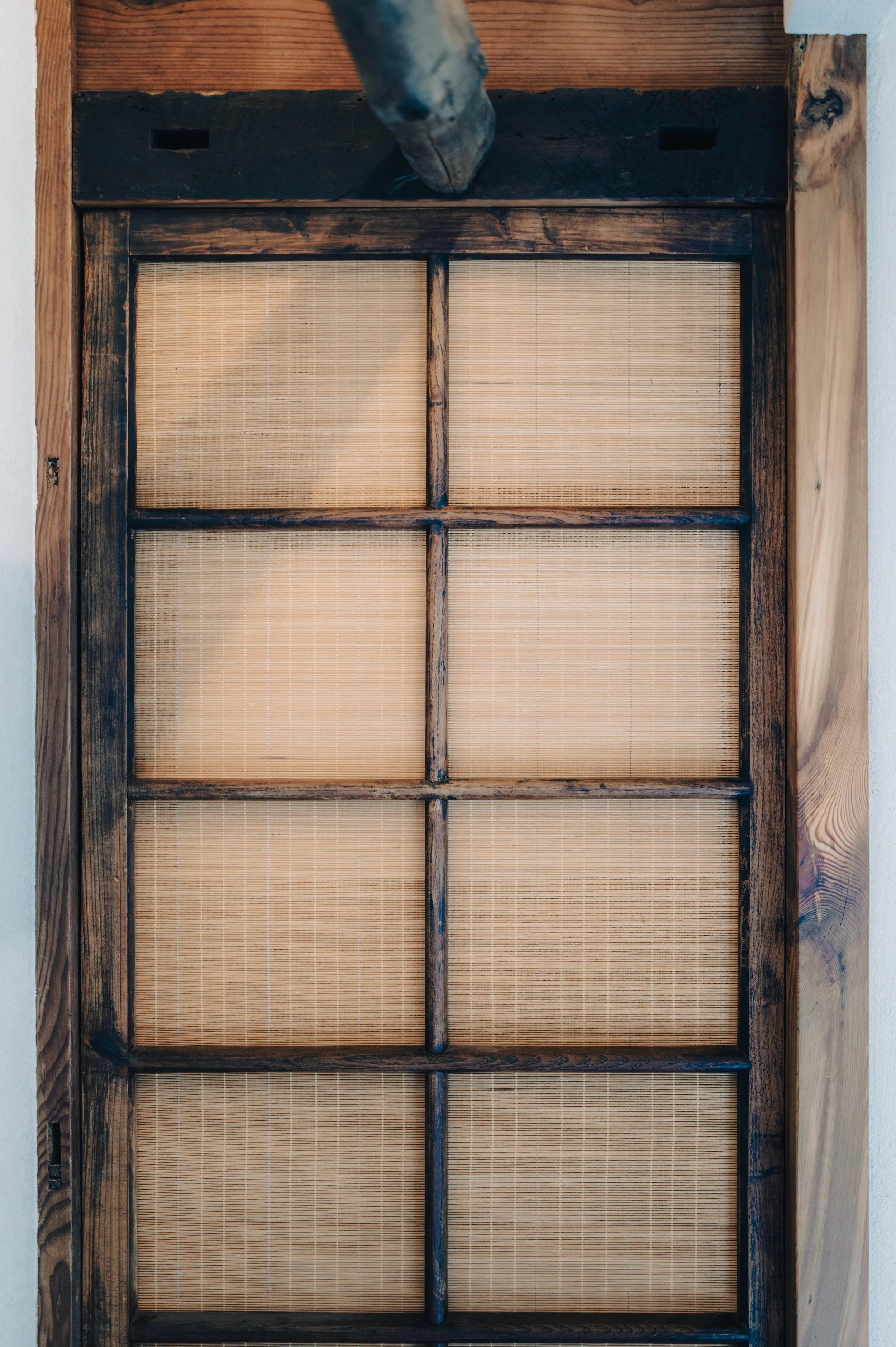 NUUT Aewol 눗애월 A wooden door with six glass panels and bamboo shades.