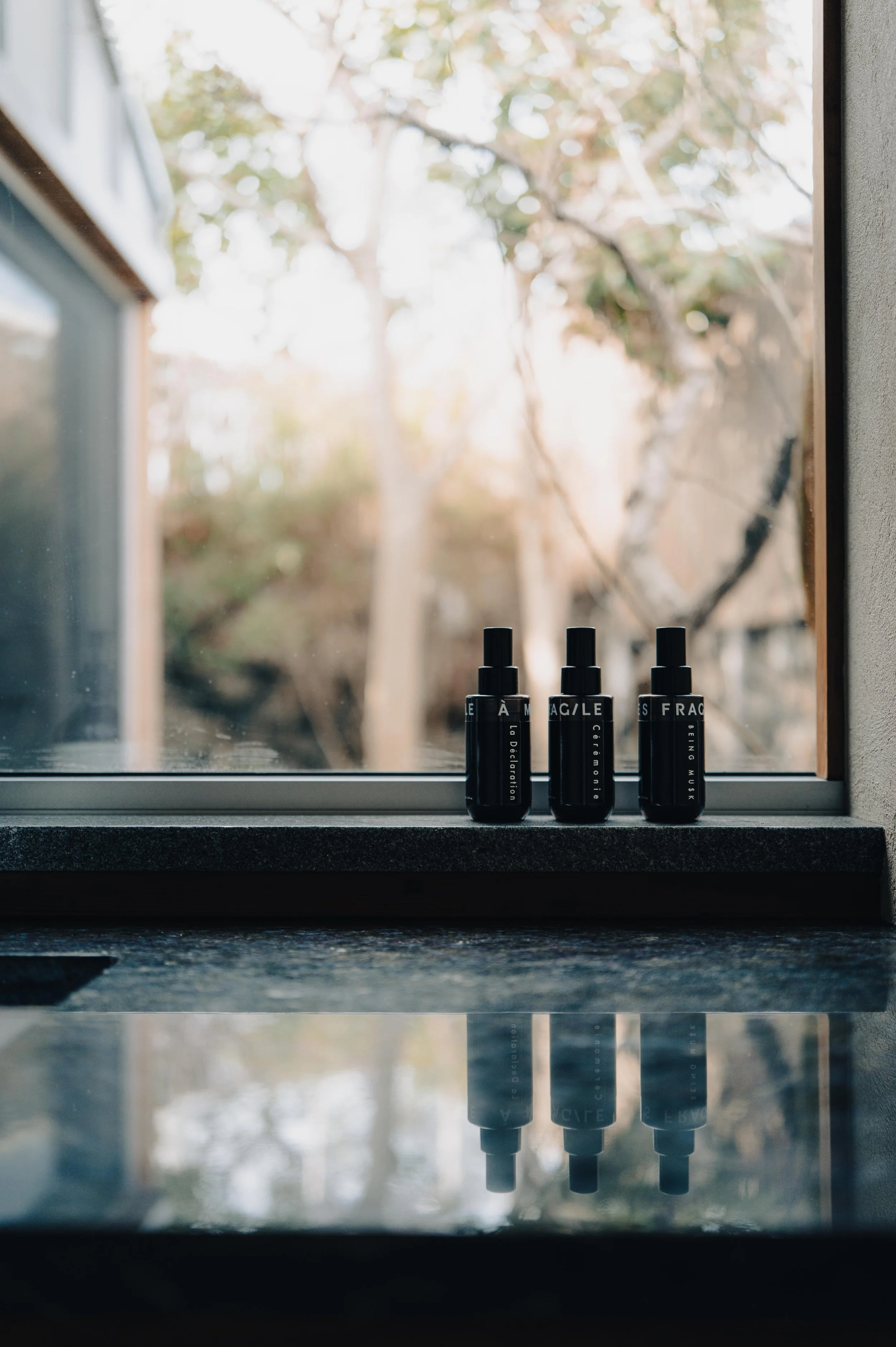 NUUT Aewol 눗애월Three black spray bottles with white text on a windowsill, with trees visible outside through the window.