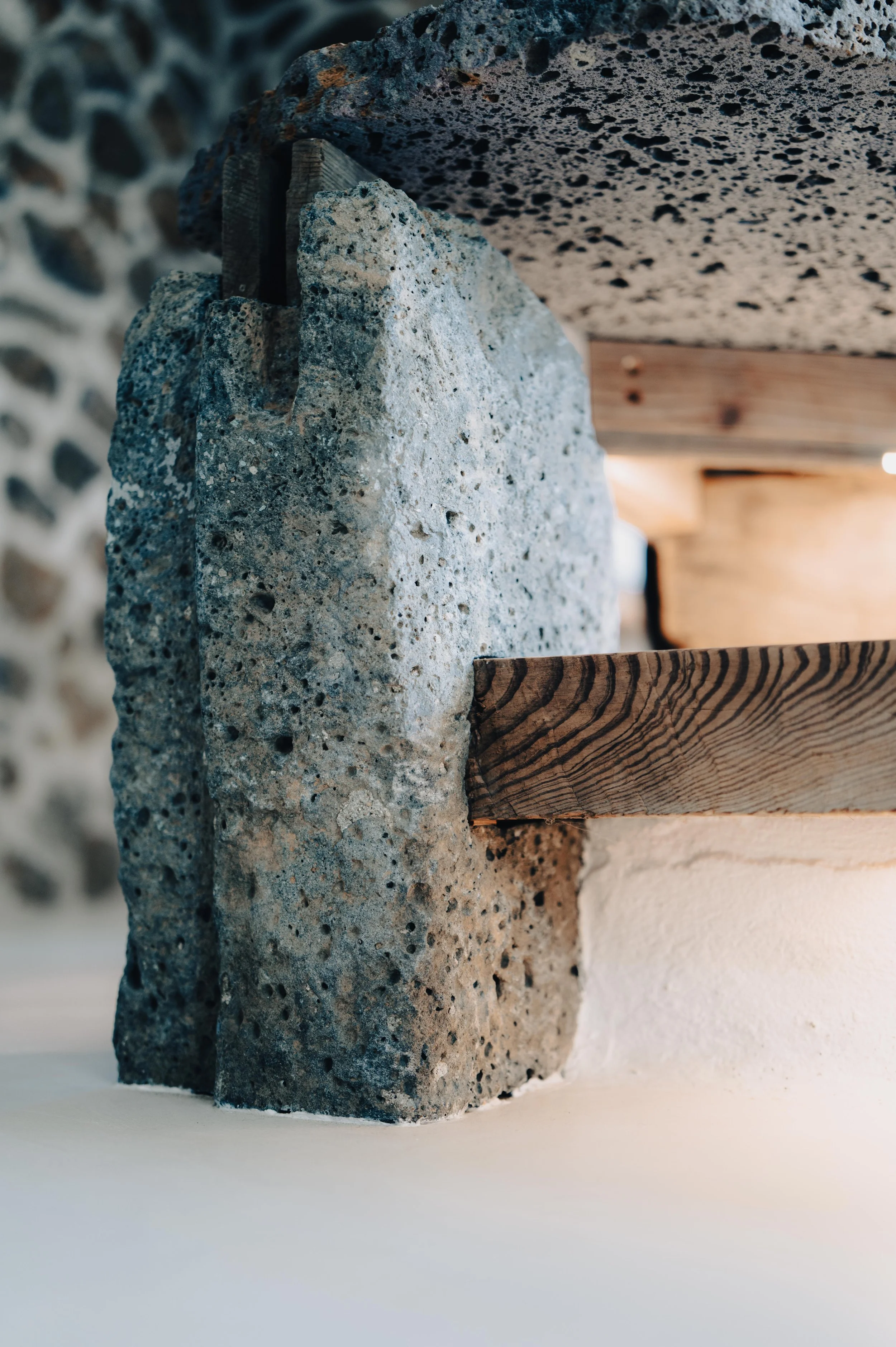 NUUT Aewol 눗애월 Close-up of a concrete and wooden structure with textured concrete and a wood beam, in an interior setting.