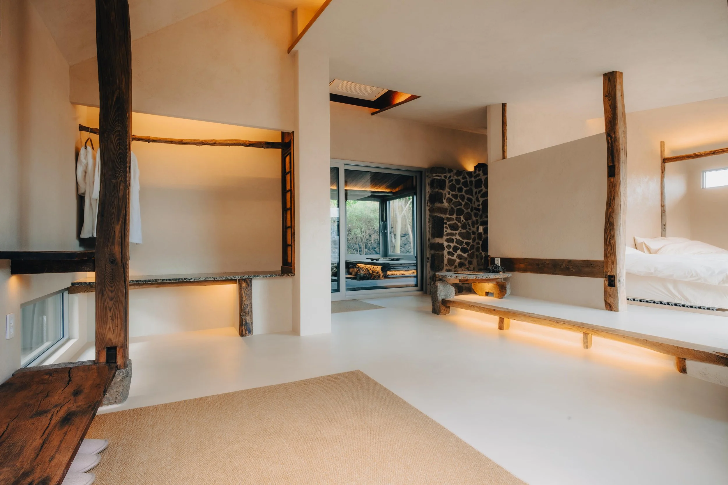 NUUT Aewol 눗애월 Modern interior of a minimalist bedroom with wooden accents, a bed, and a sliding door leading outside.