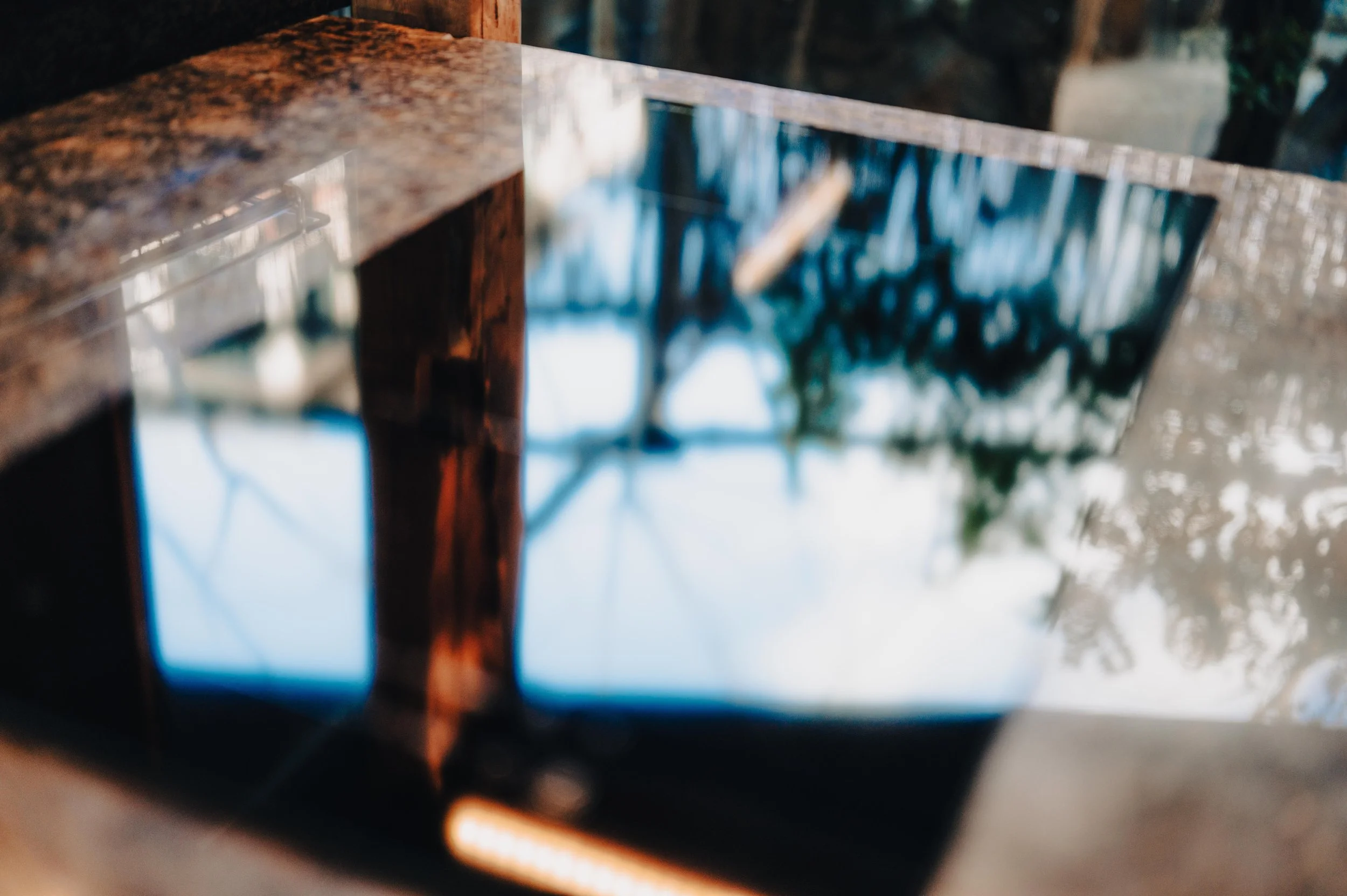 NUUT Aewol 눗애월 Close-up of a black induction cooktop with a reflection of the sky, trees, and outdoor structures on its surface.
