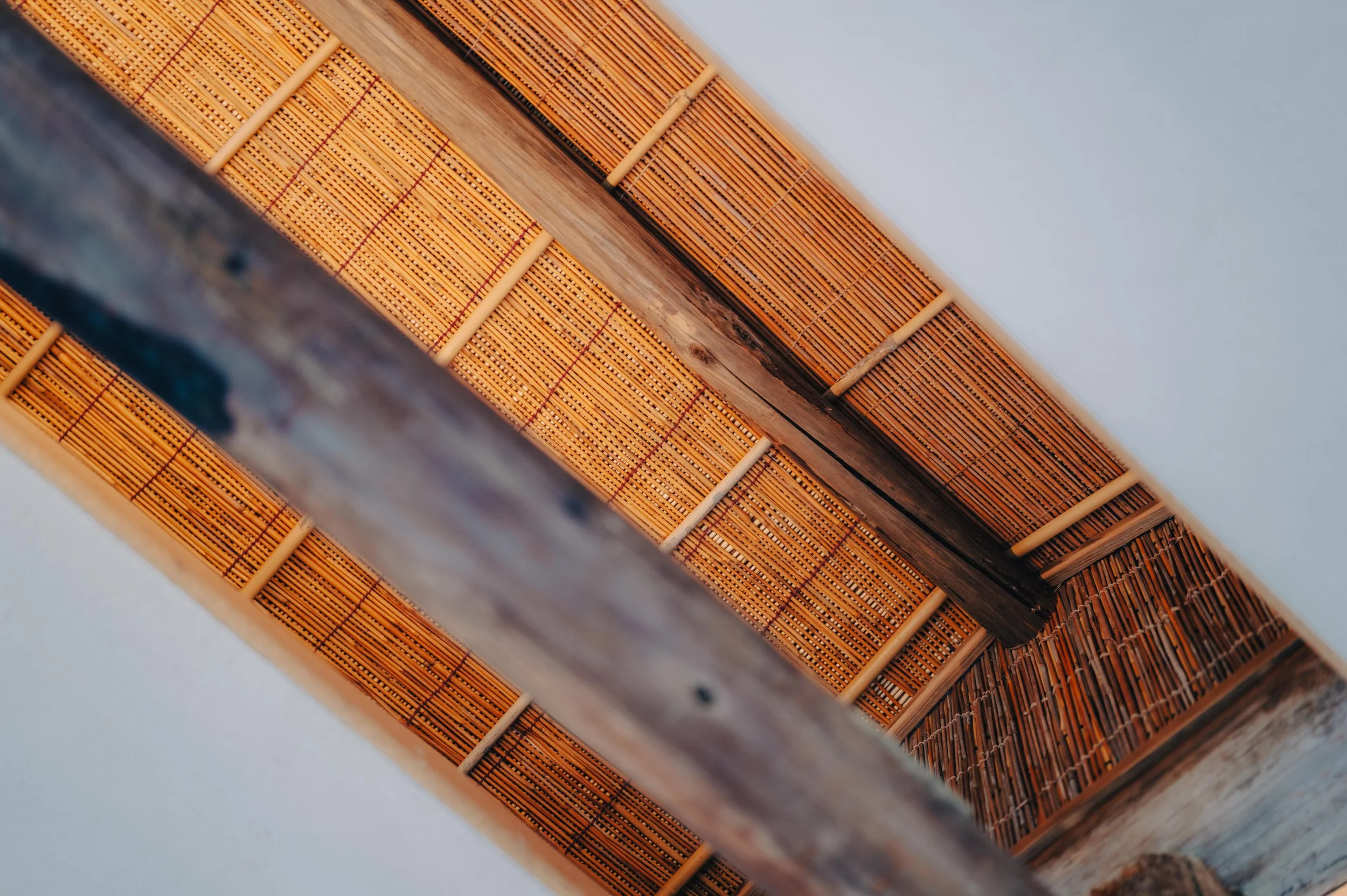 NUUT Aewol 눗애월 Close-up view of a bamboo and wood ceiling with wooden supports and an adjacent wooden railing.