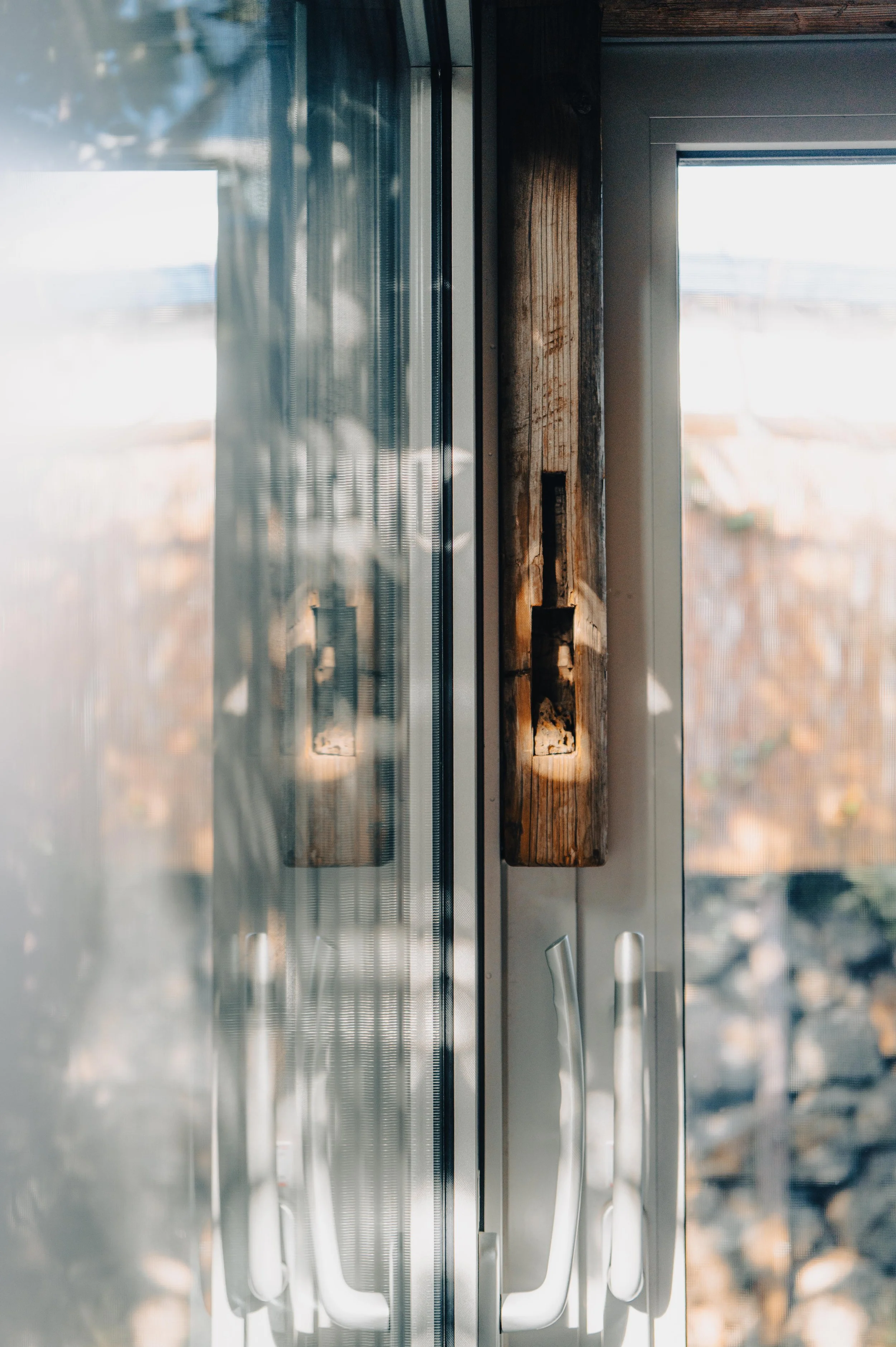 Close-up of a wooden beam with a rectangular notch cut out, mounted between a glass door and window in a building.