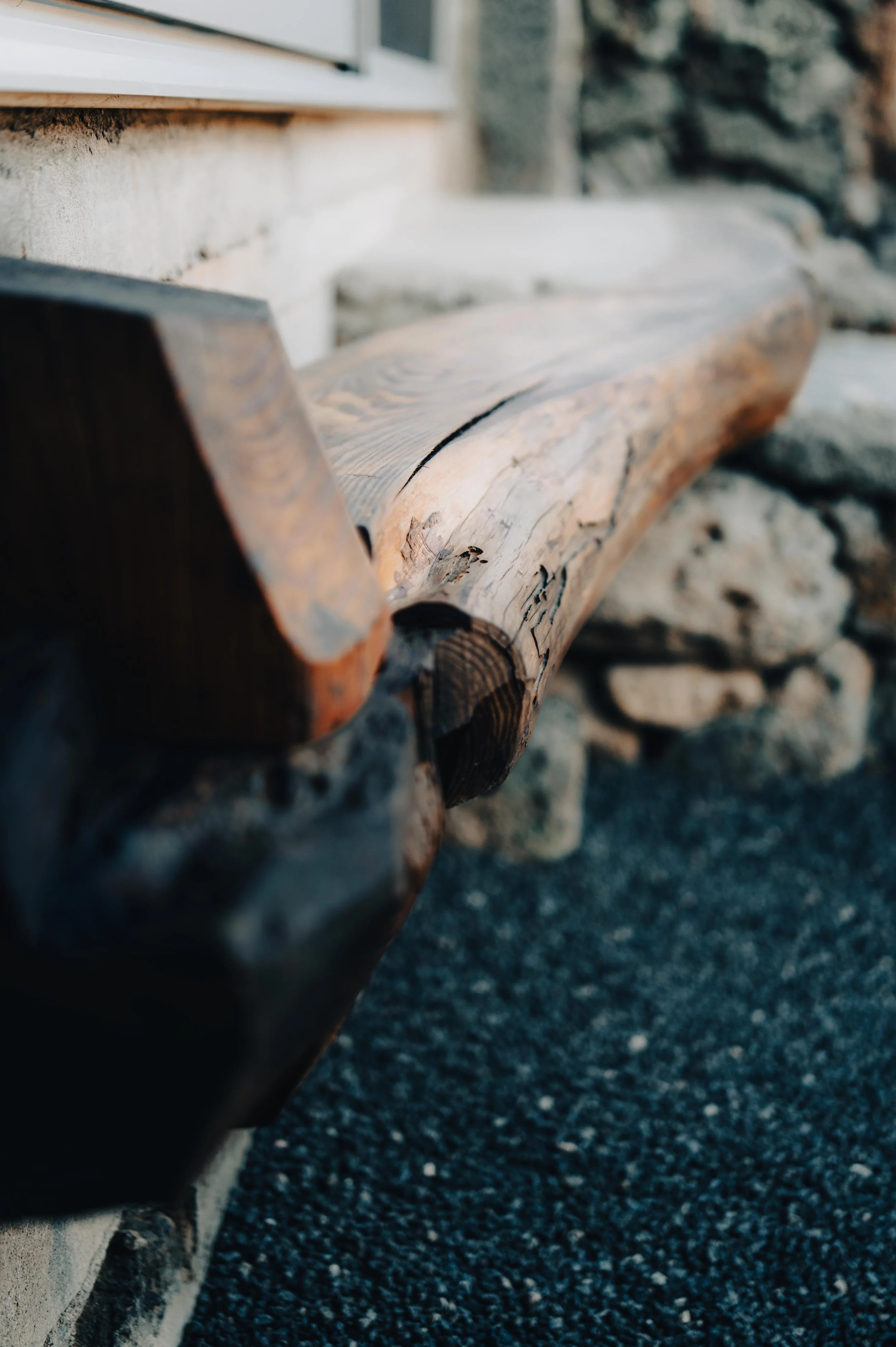Close-up of a rustic wooden bench made from a single piece of wood, placed outside against a stone wall.
