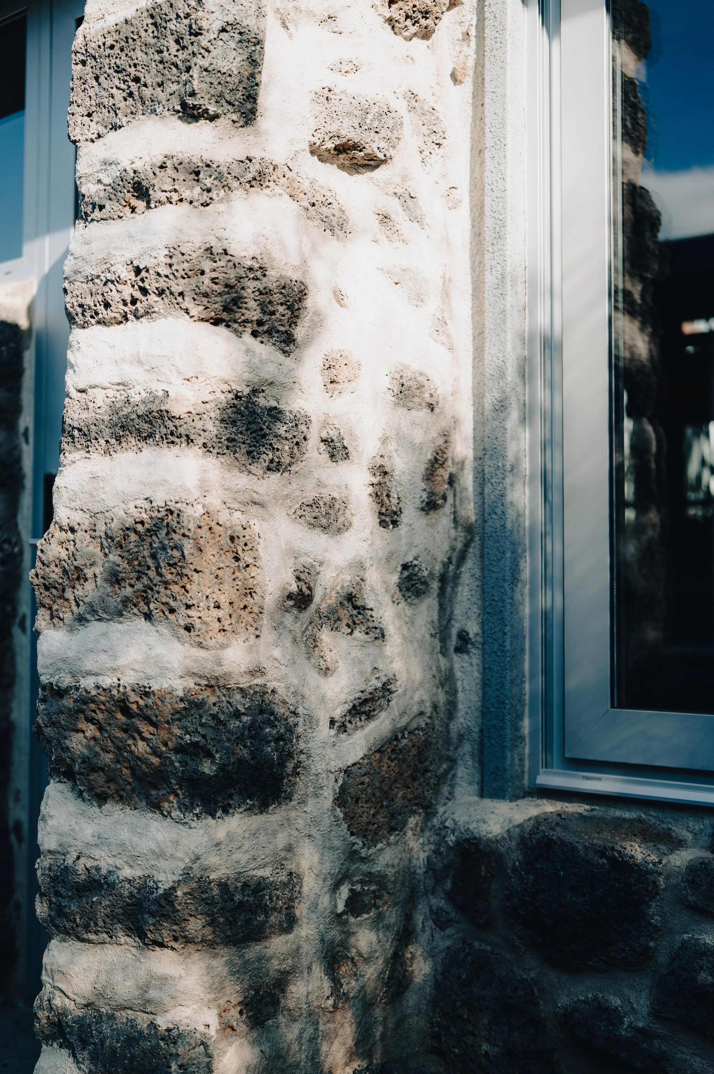 Close-up of a stone wall with white mortar, situated next to a window with a metal frame.