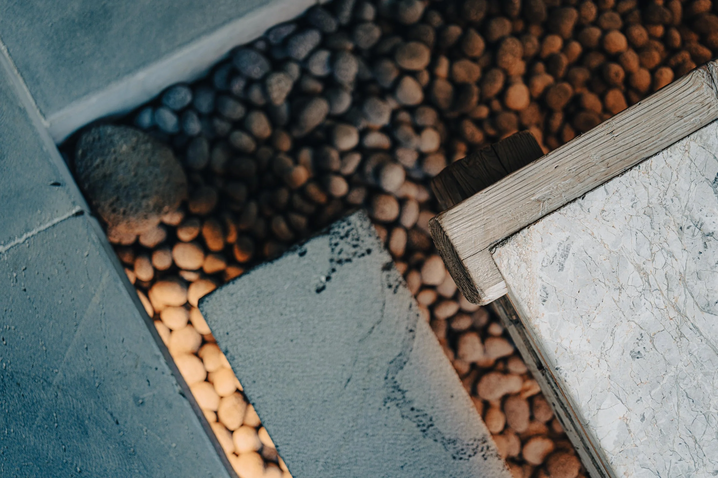 Close-up of a corner with cinder blocks, pebbles, and a wooden edge of a piece of furniture or structure.