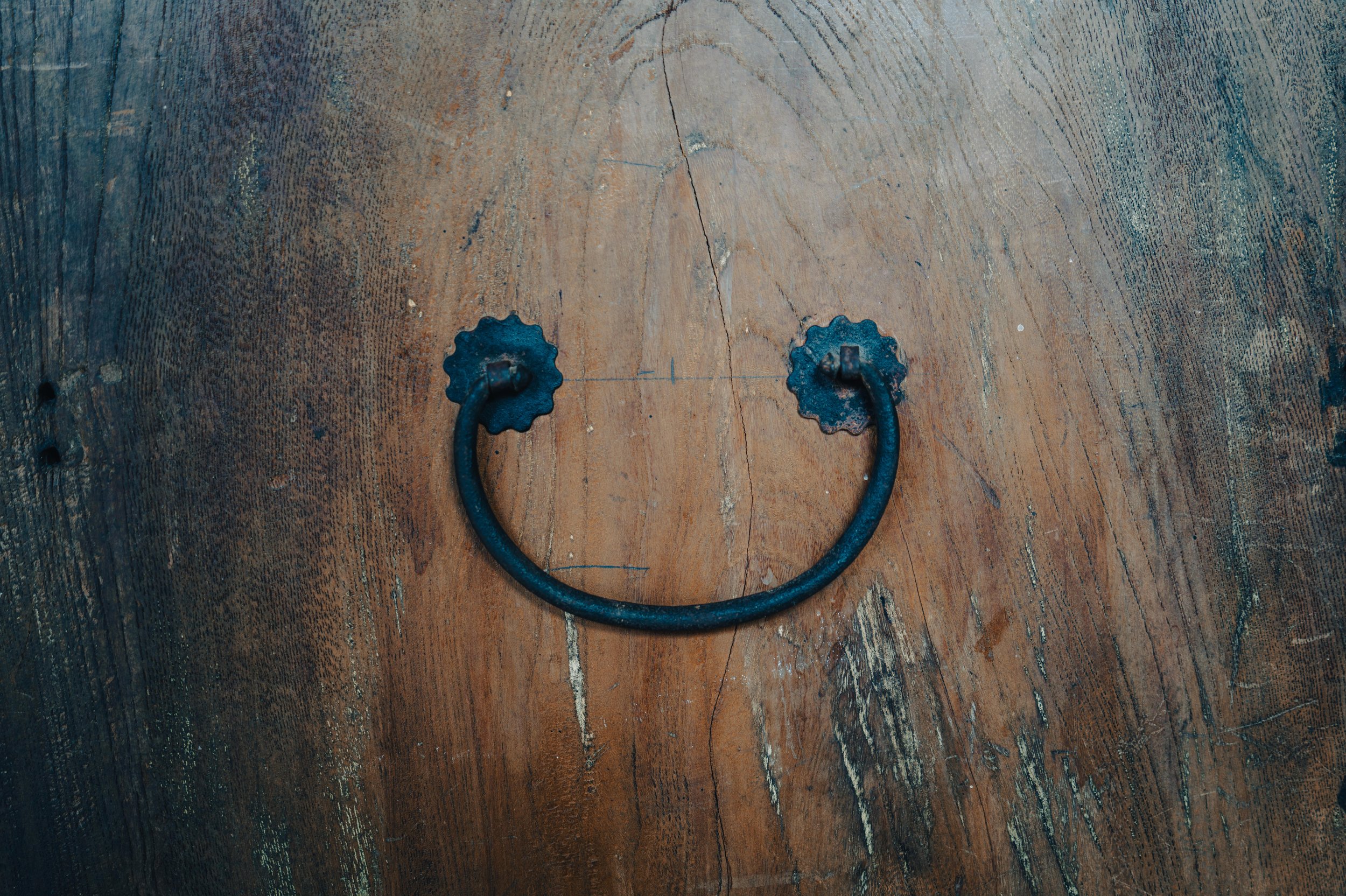 NUUT Aewol 눗애월 A vintage black metal drawer pull or handle shaped like a smiling face on a wooden surface.