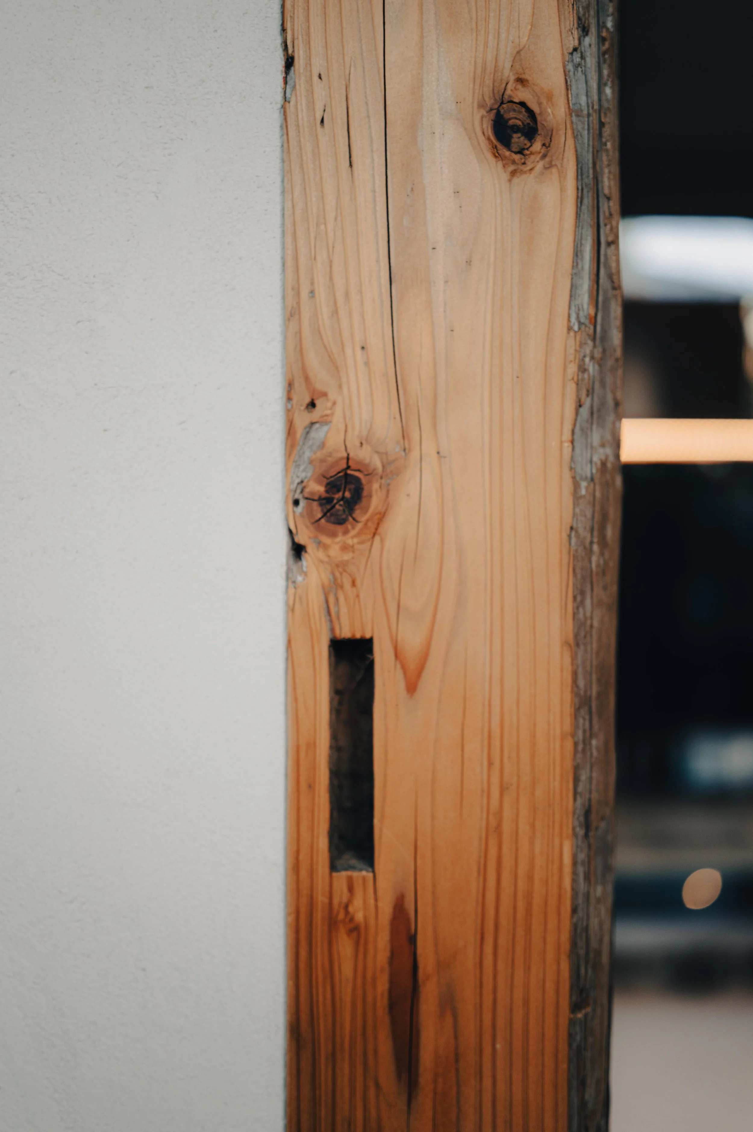 NUUT Aewol 눗애월 Close-up of a wooden wall framing with visible knots and a rectangular hole, next to a textured white wall.