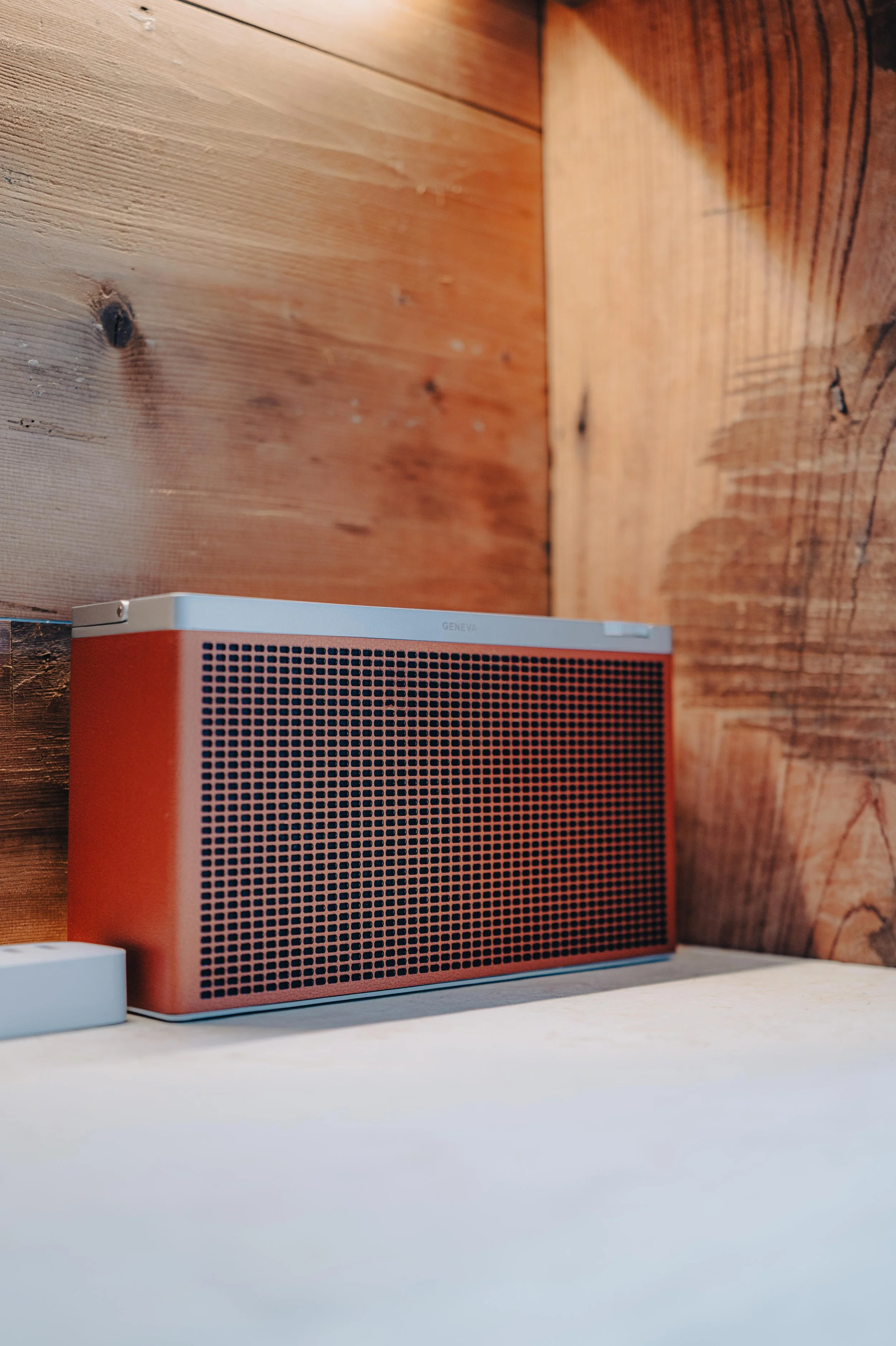 NUUT Aewol 눗애월 A rectangular red and silver speaker on a white surface against a wooden wall.