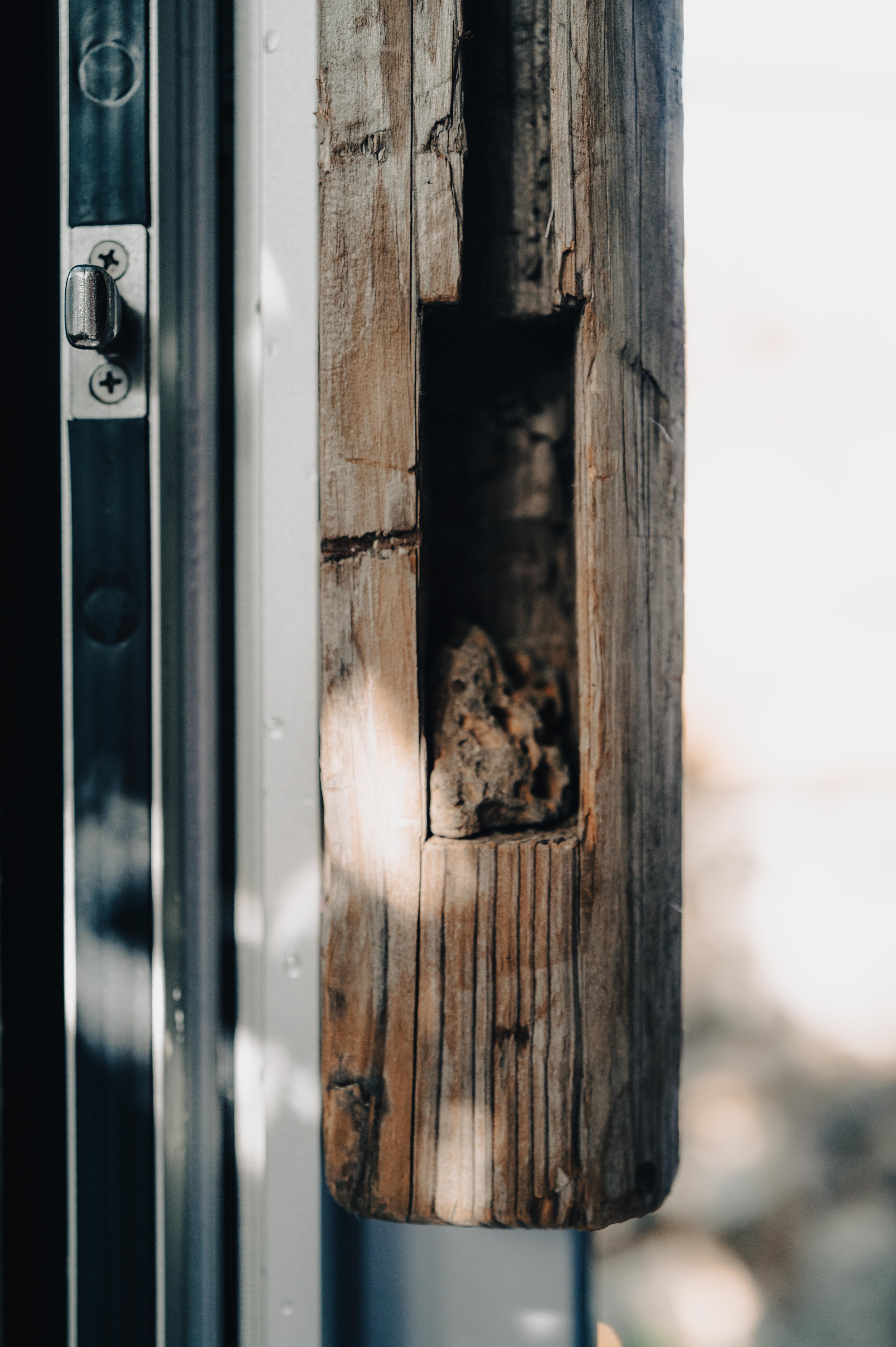 Close-up of a wooden frame with a rectangular hole, next to a metal door frame and door latch.