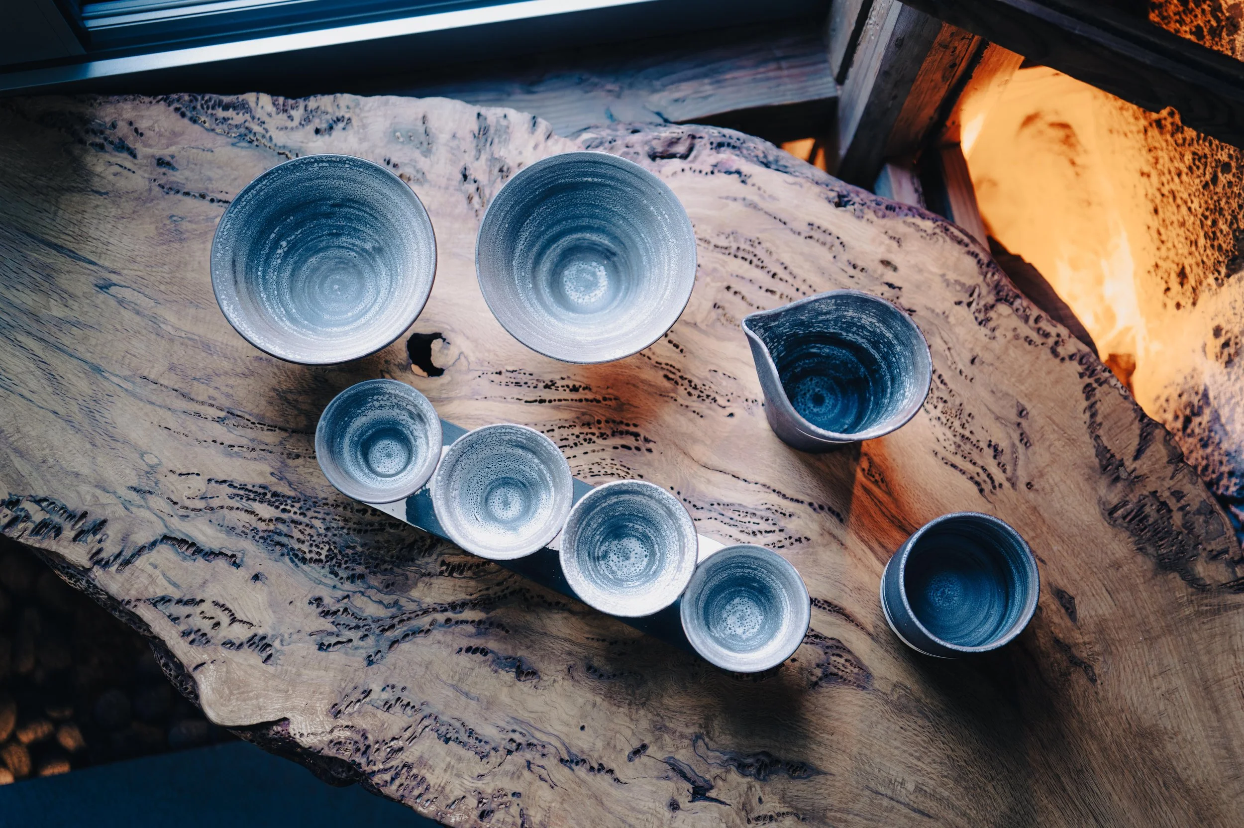 Ceramic bowls and cups with blue and gray swirl designs arranged on a rustic wooden table.