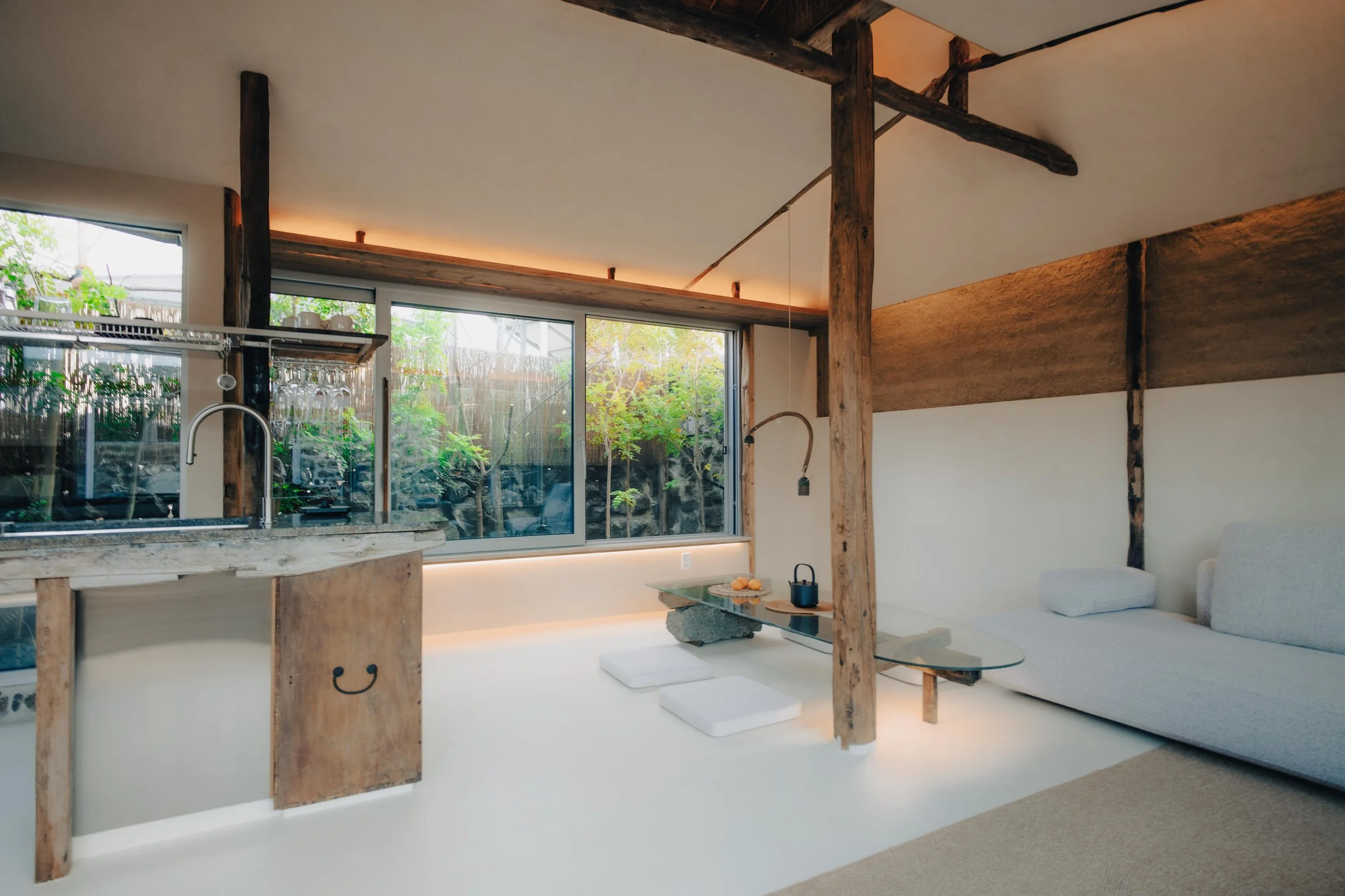 NUUT Aewol 눗애월 Modern living space with a kitchenette, large window overlooking greenery, and a sitting area with a white sofa and low table.