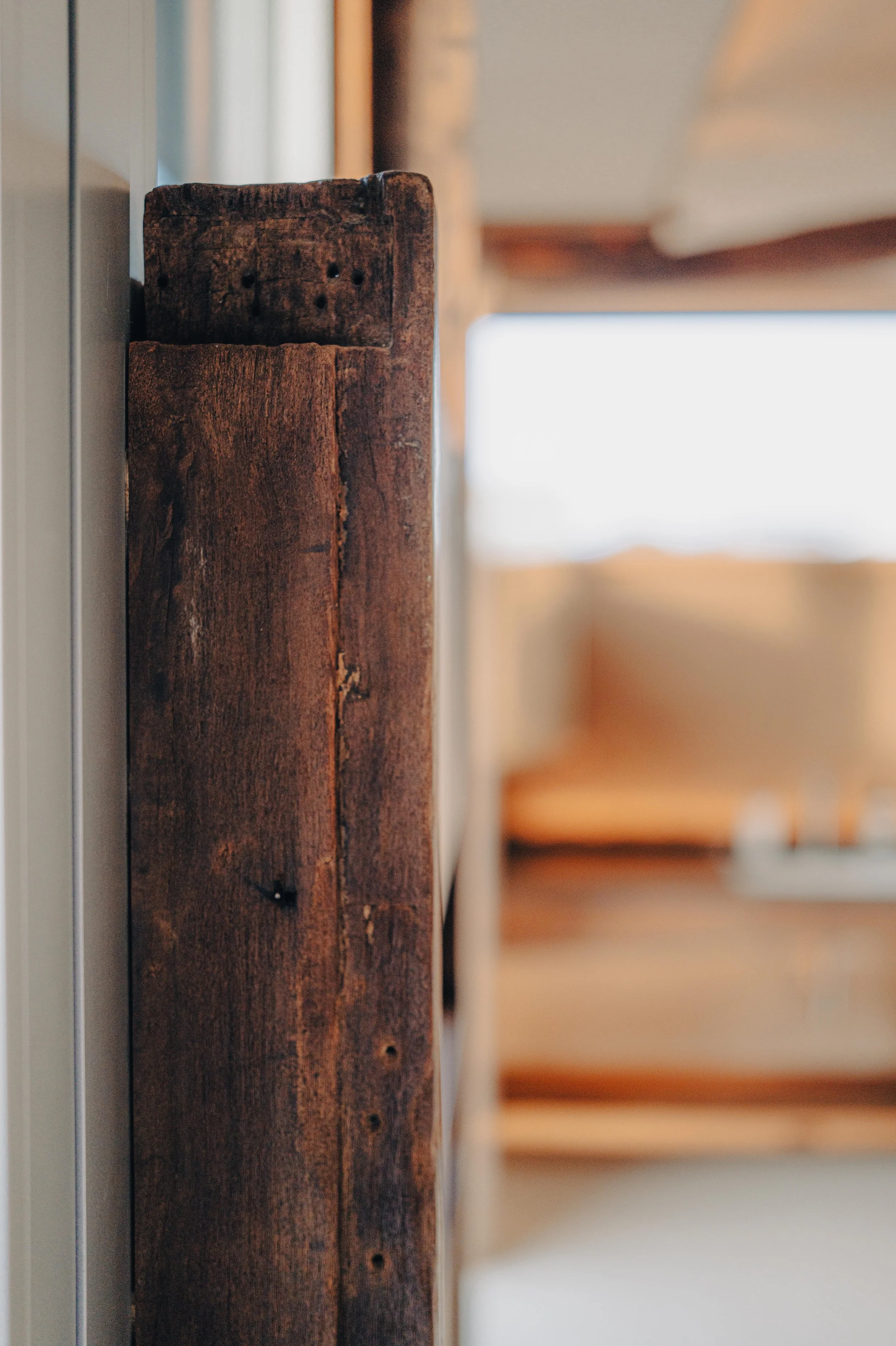 NUUT Aewol 눗애월 Close-up of a weathered wooden beam in a rustic interior, with a blurred background.