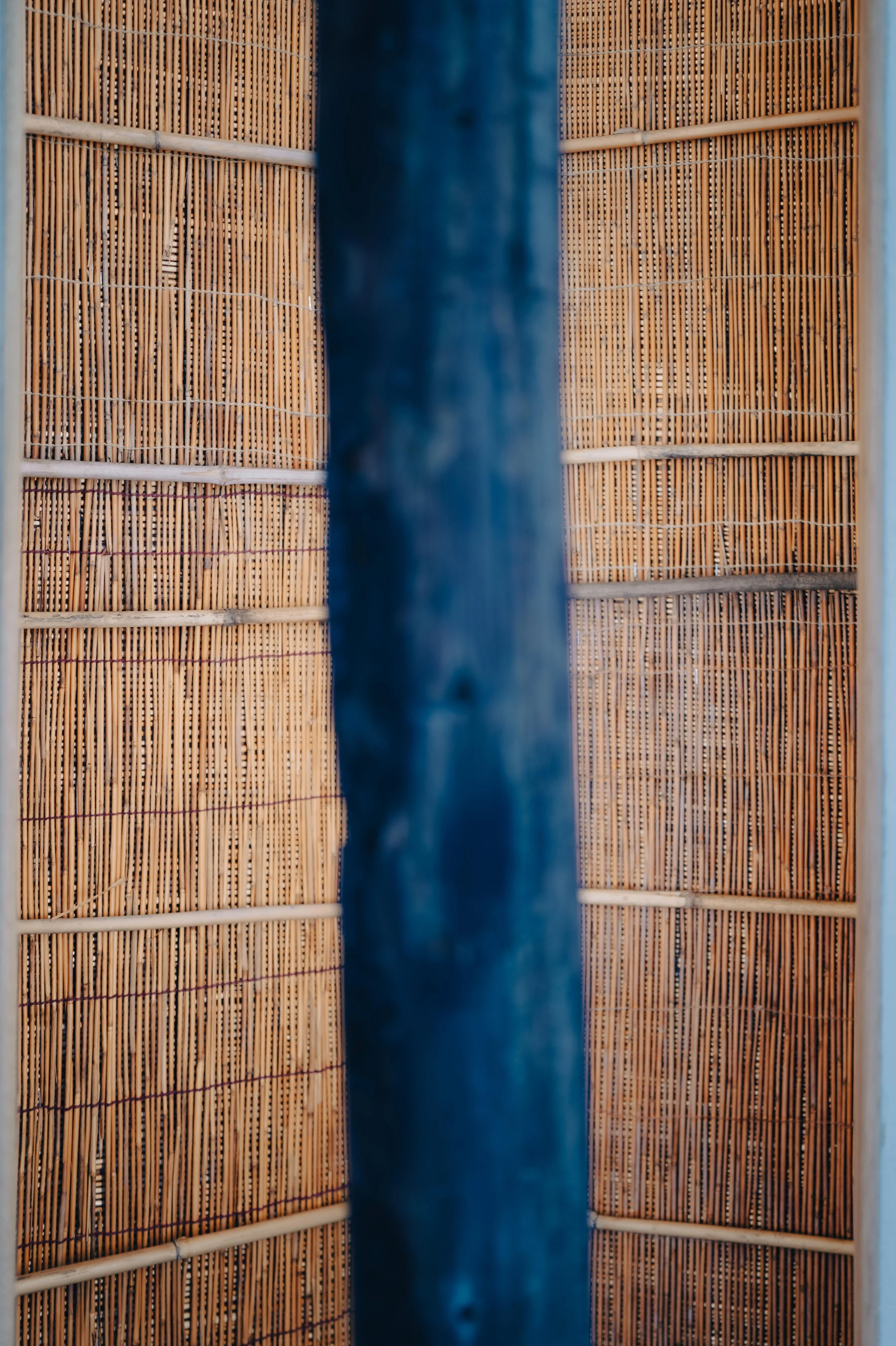 NUUT Aewol 눗애월Close-up view of bamboo blinds divided by a blue wooden post.