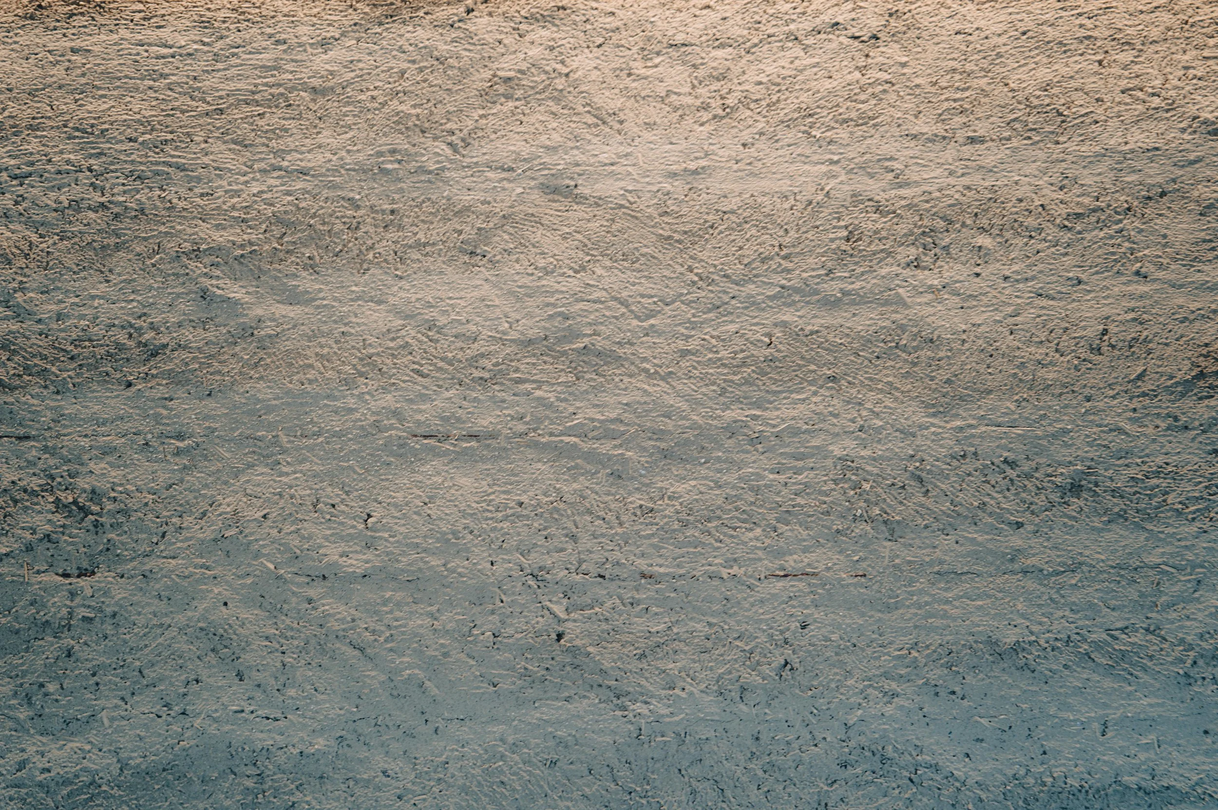 NUUT Aewol 눗애월 Close-up of a textured, sandy surface with light and shadow playing across it.