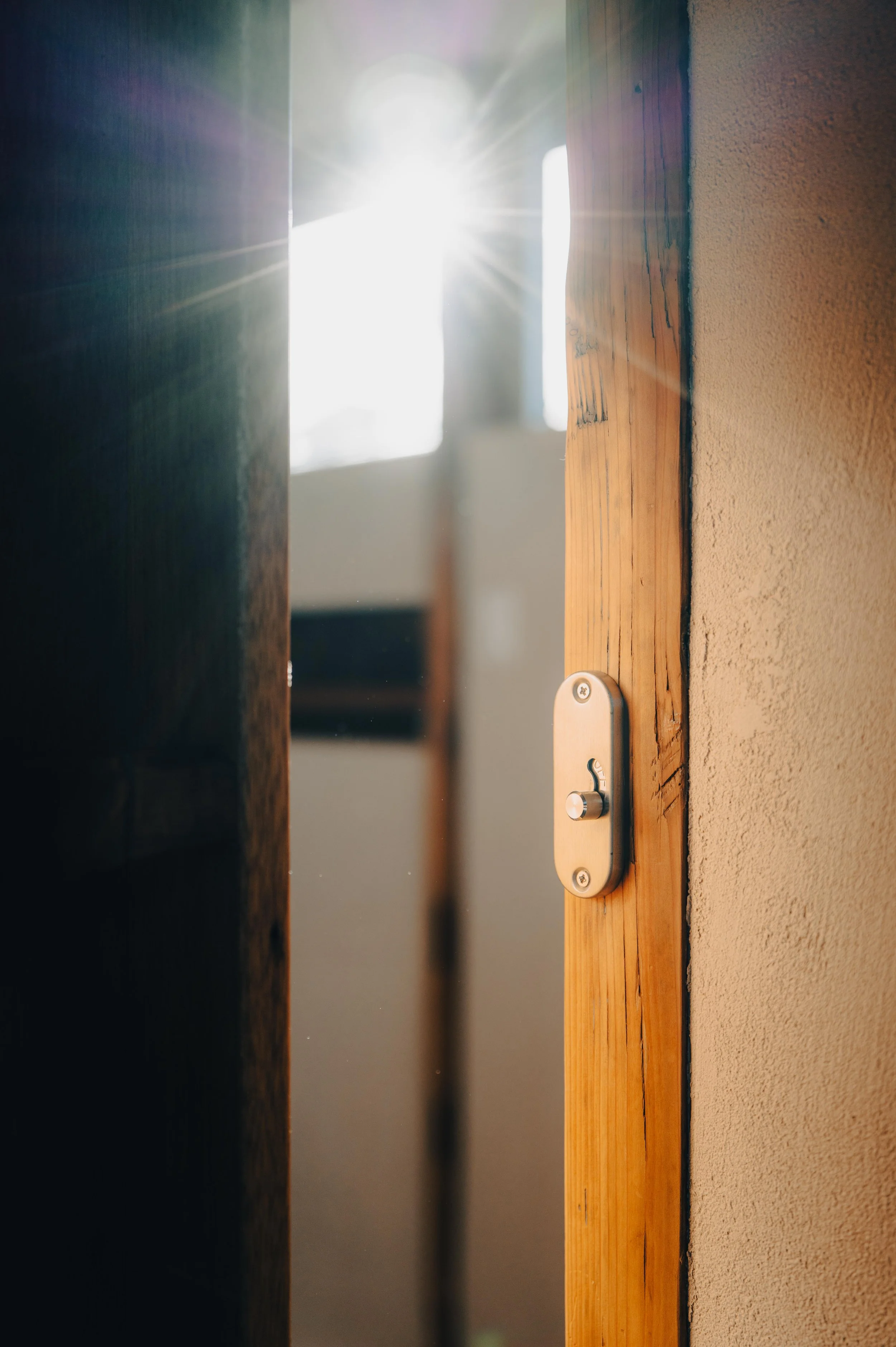 NUUT Aewol 눗애월 A door latch on a wooden door frame with sunlight shining through the gap.