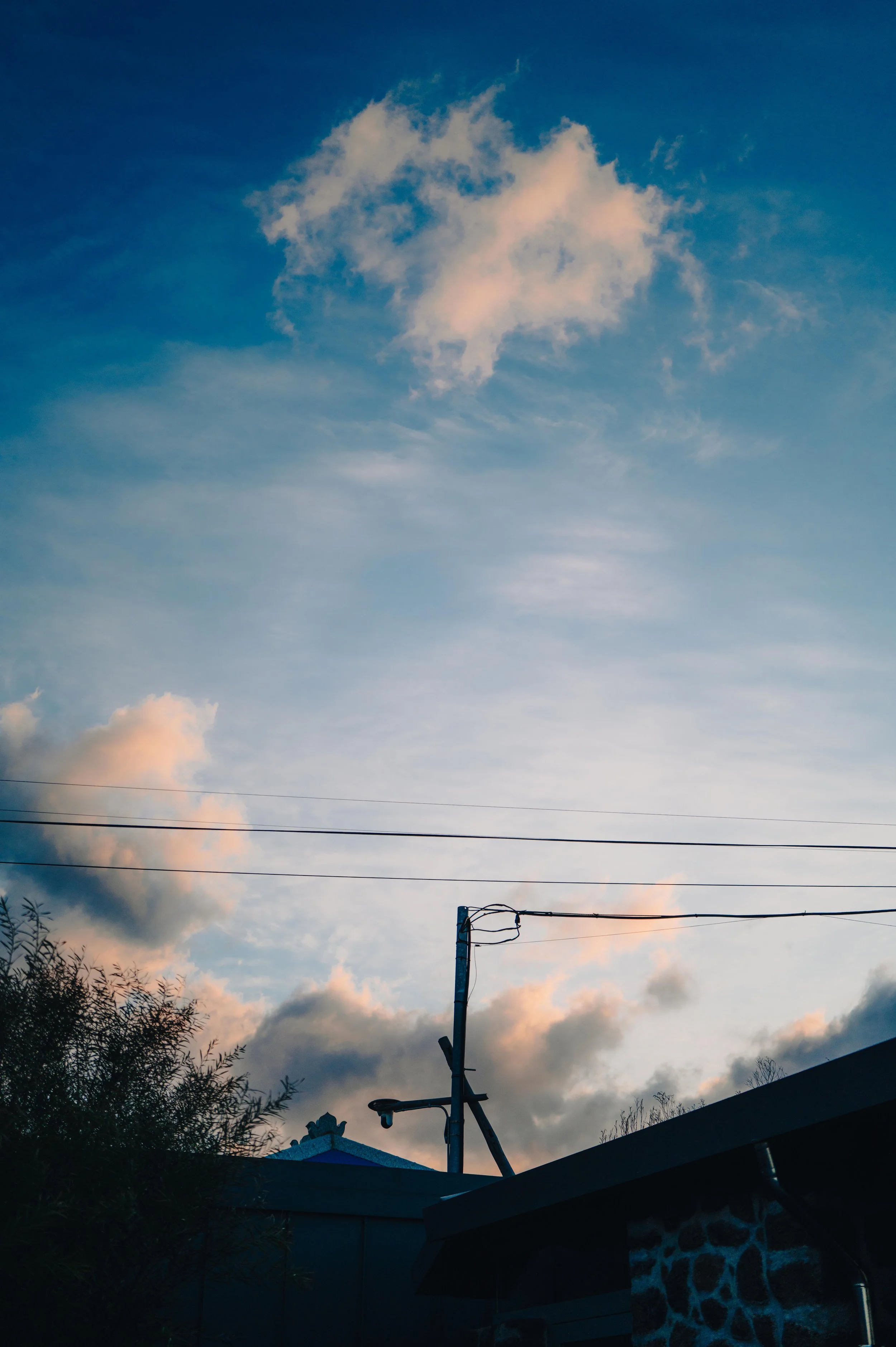 NUUT Aewol 눗애월 Sky with scattered clouds and a utility pole with wires in the foreground, along with a building roof and trees.