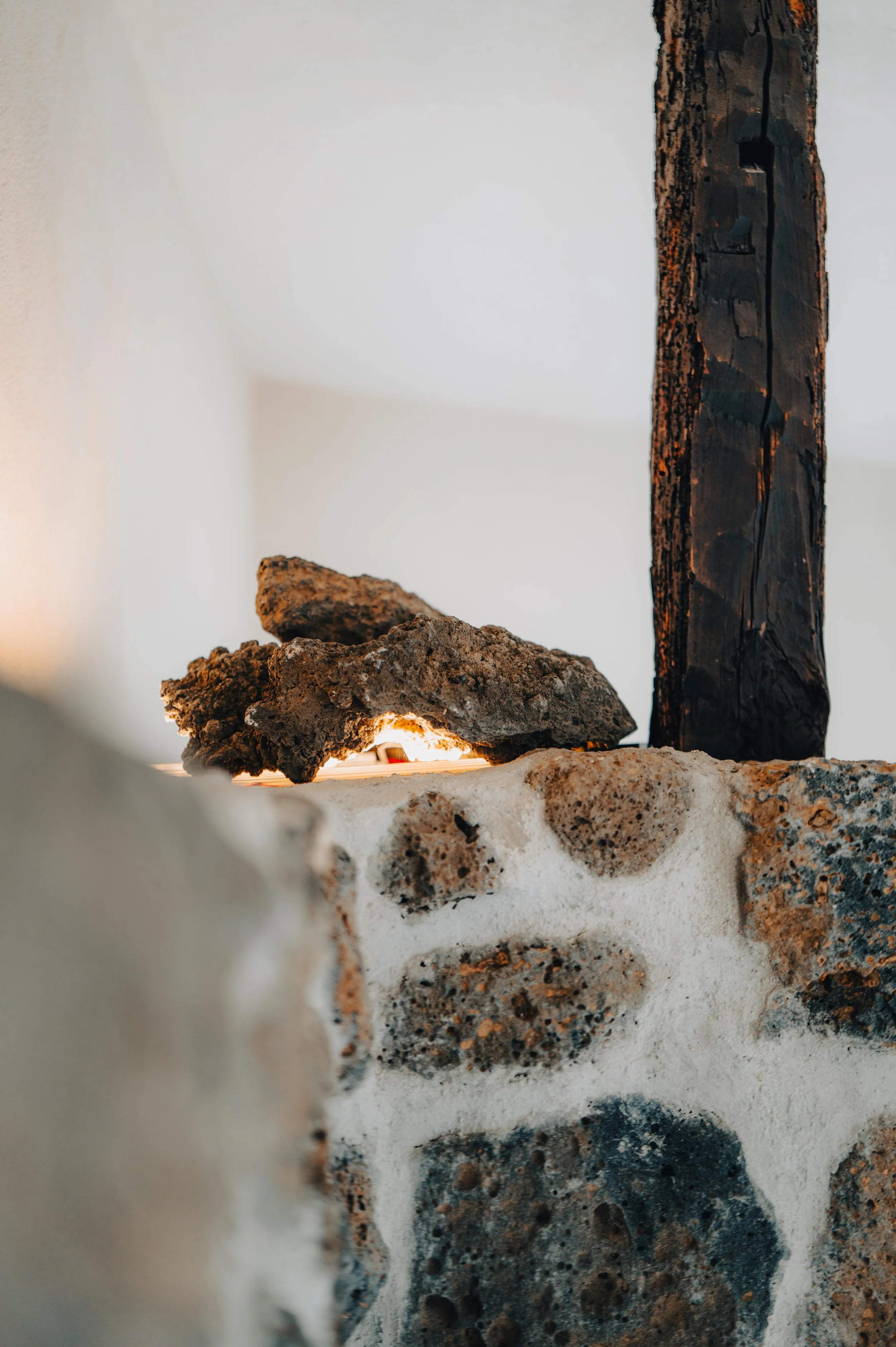 NUUT Aewol 눗애월 Close-up photo of a textured stone wall with a blackened wooden post or beam in the background.