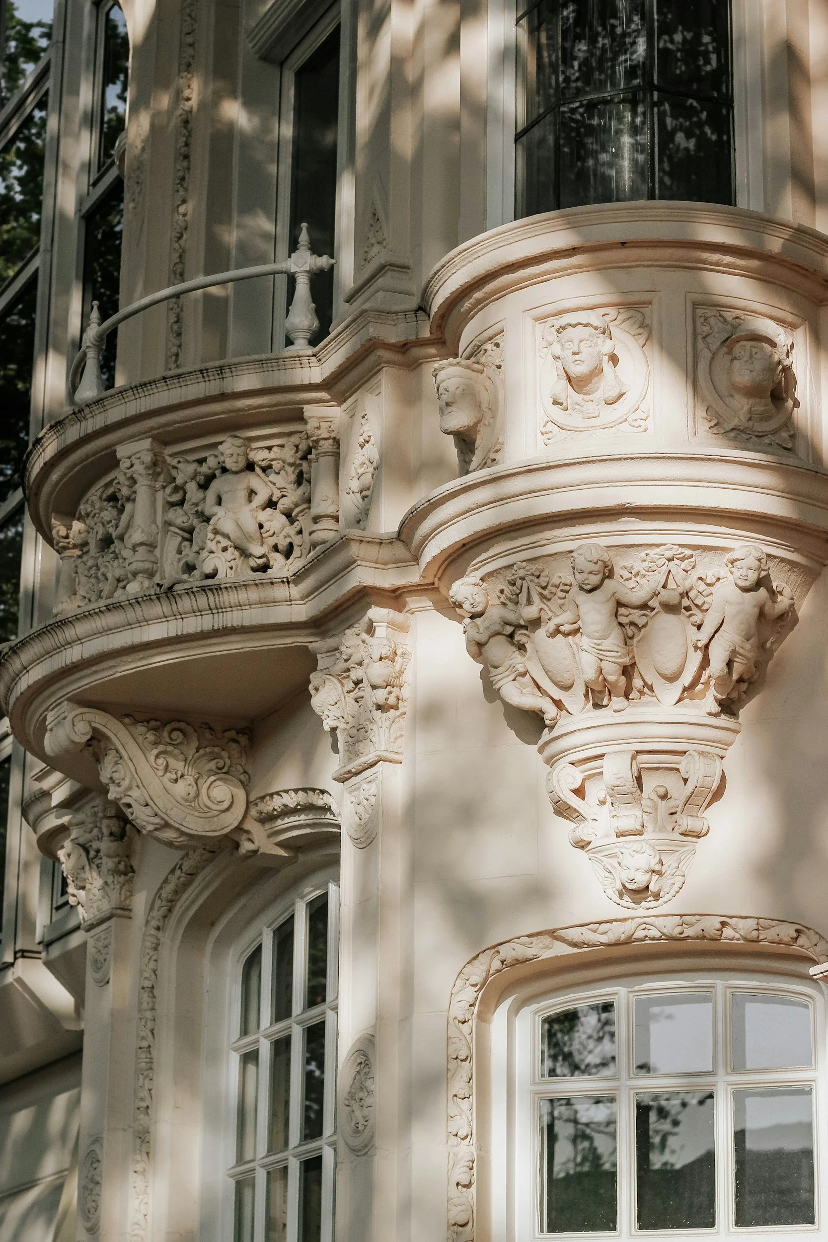 Close-up of ornate building facade with intricate stone carvings, cherubs, human faces, and decorative scrollwork around windows.