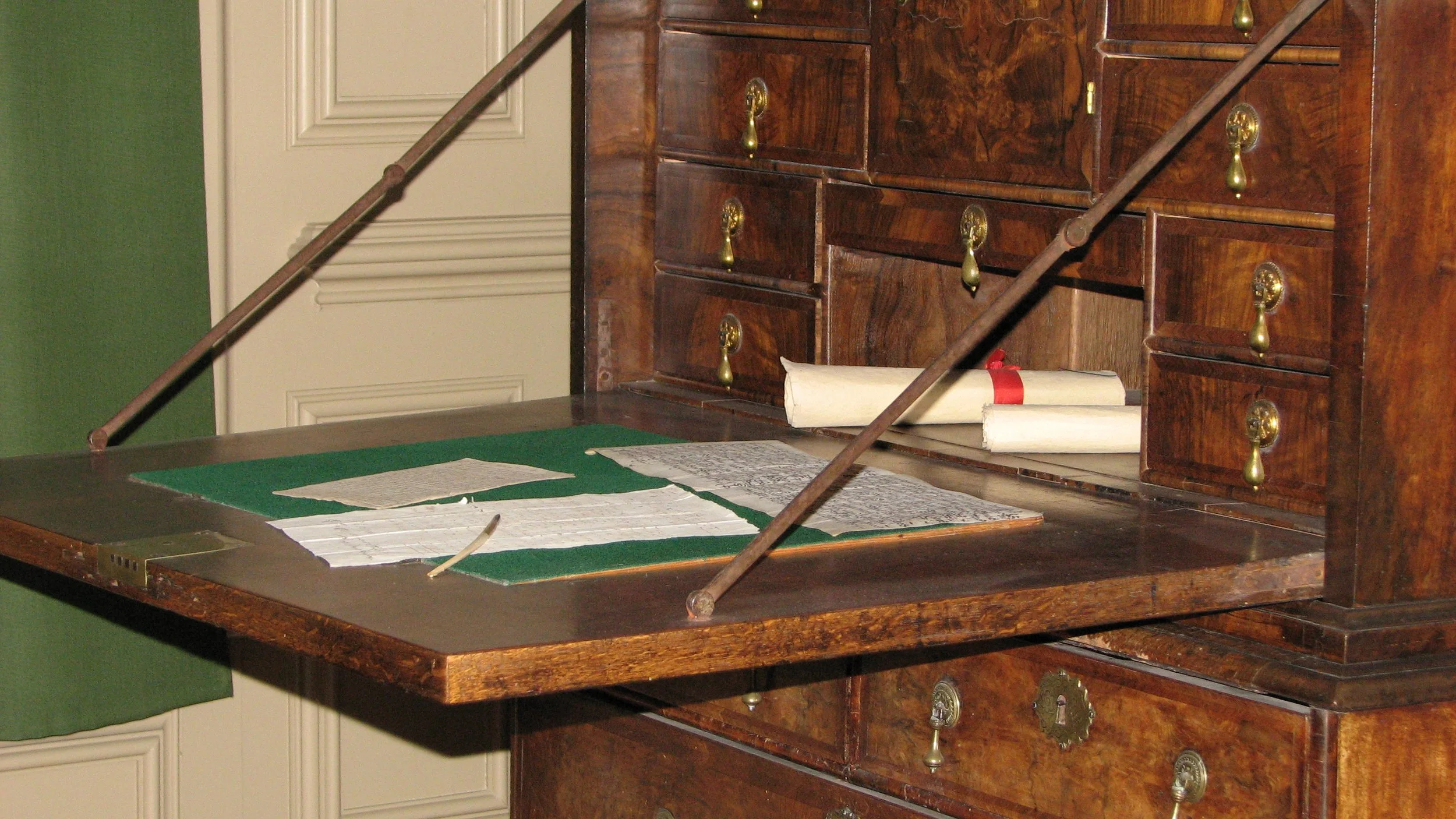 An old-fashioned writing desk with felt pad, quill pen, and drawers