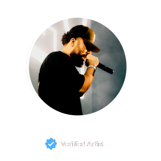 A man with a beard and brown cap holding a microphone on stage.