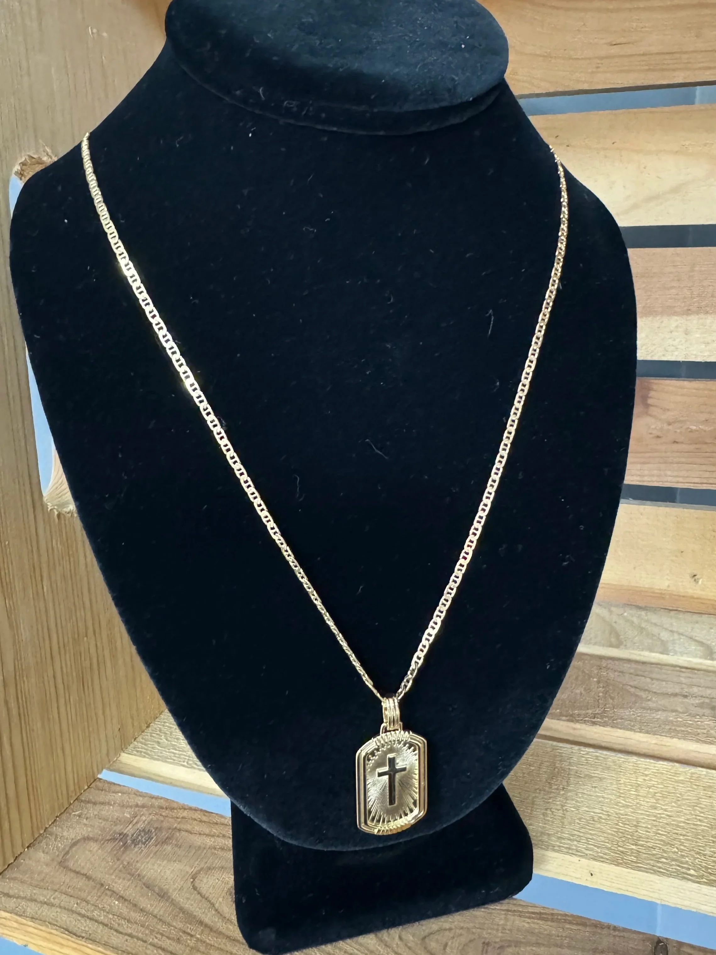 Gold chain necklace with pendant featuring a cross, displayed on a black velvet bust.