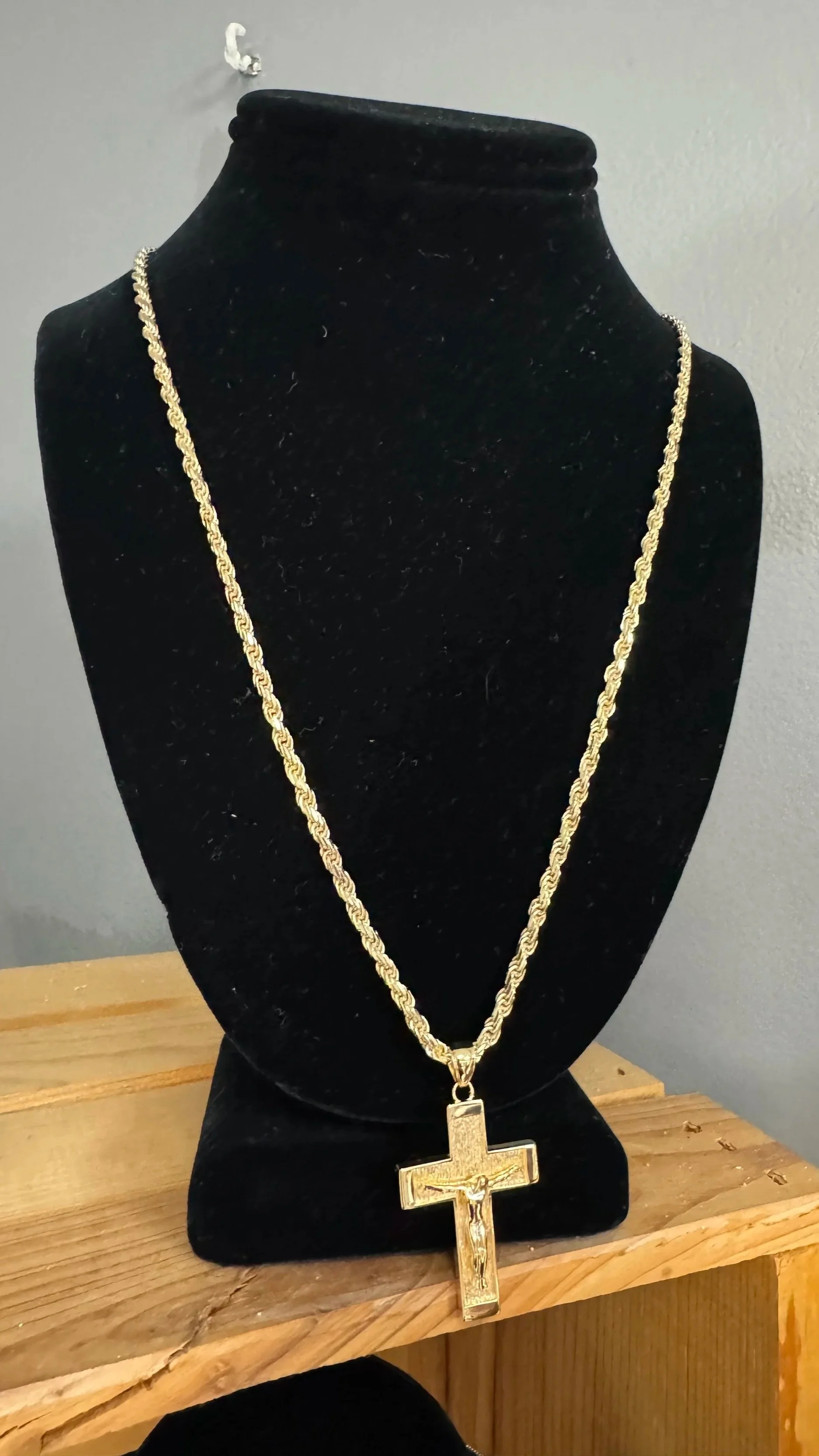 Gold chain necklace with a crucifix pendant displayed on a black velvet bust.