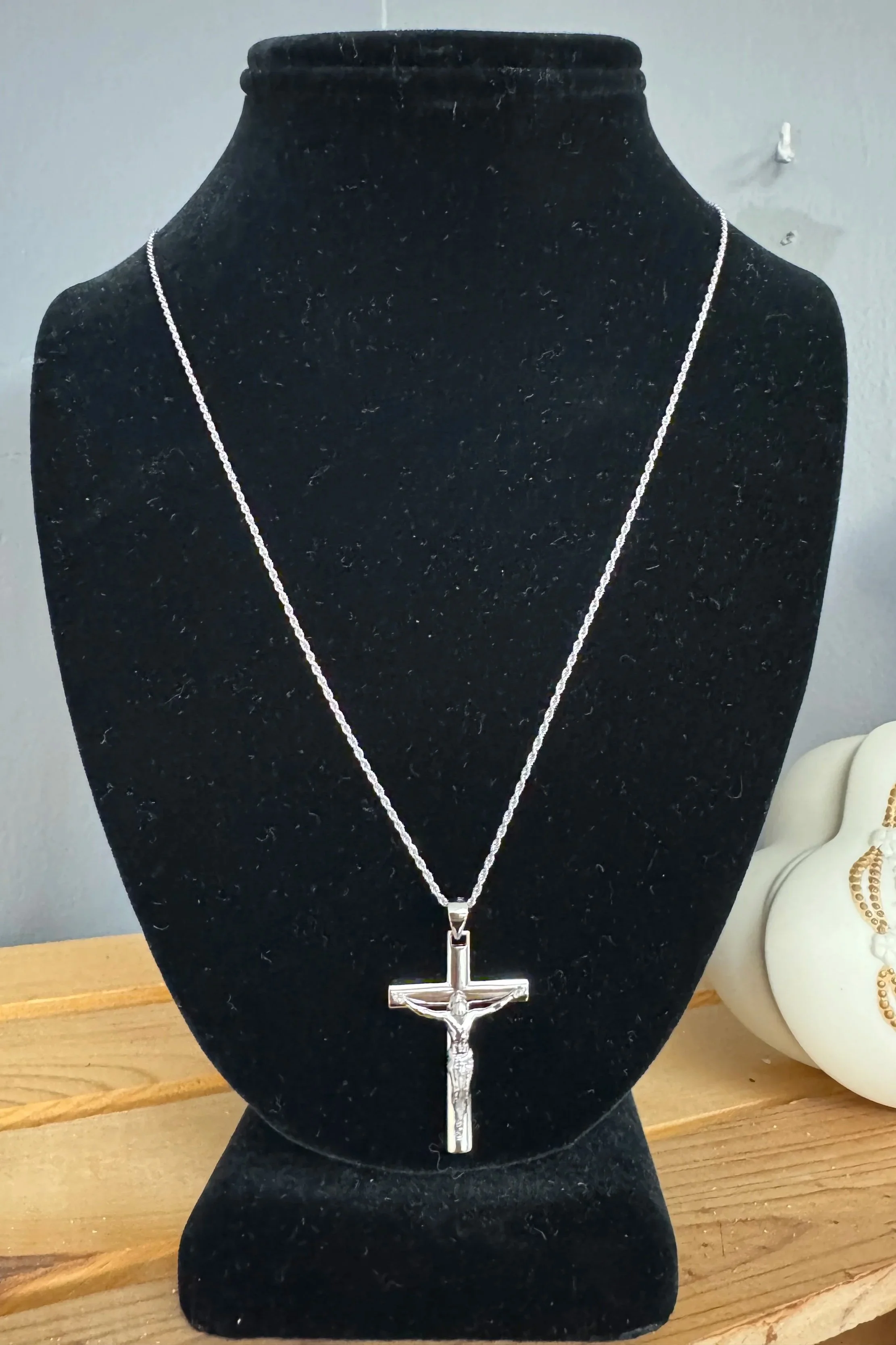 Silver necklace with a crucifix pendant on a black display bust.