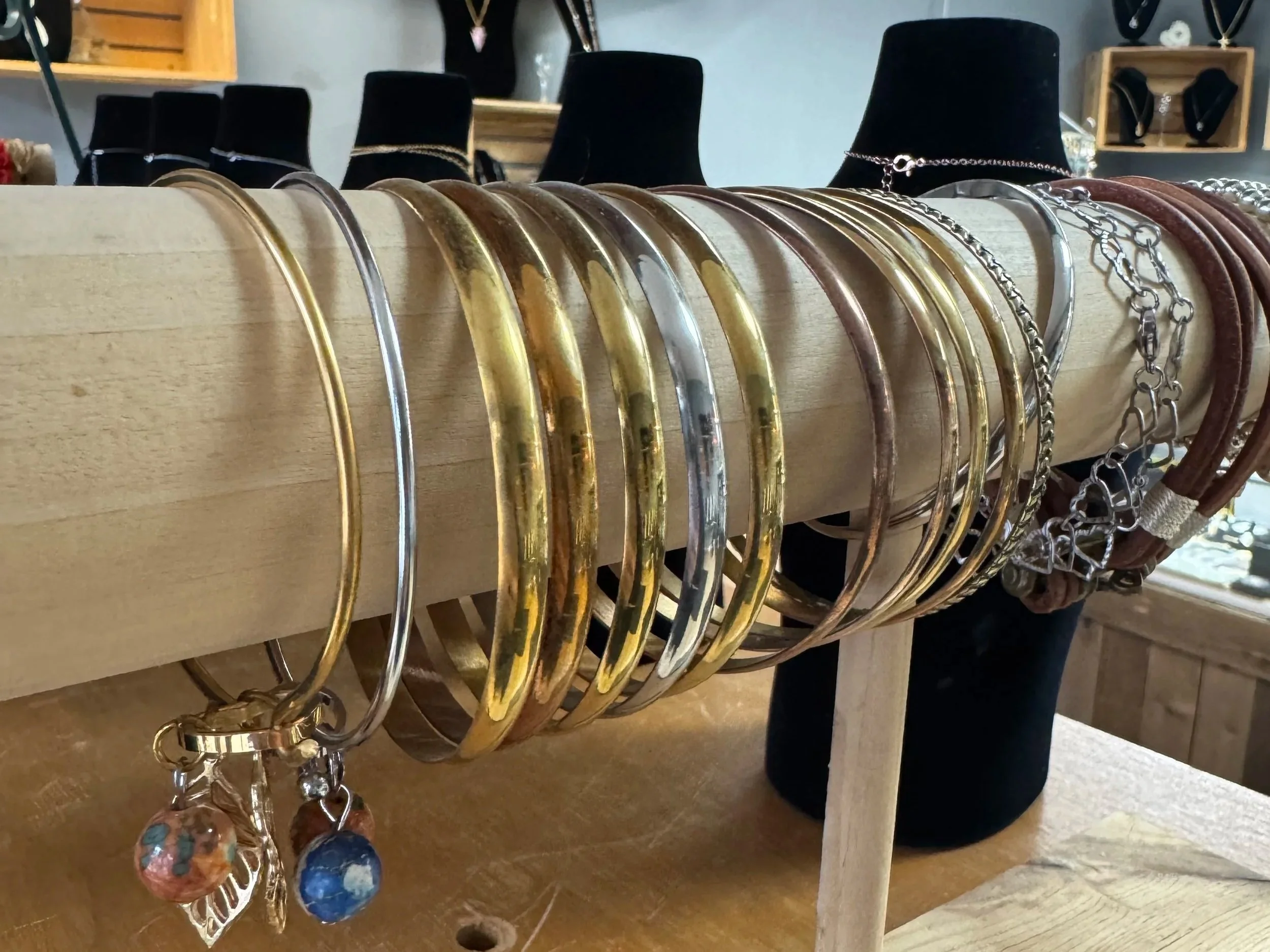 Display of various metal jewelry bracelets on a wooden rack in a jewelry store.