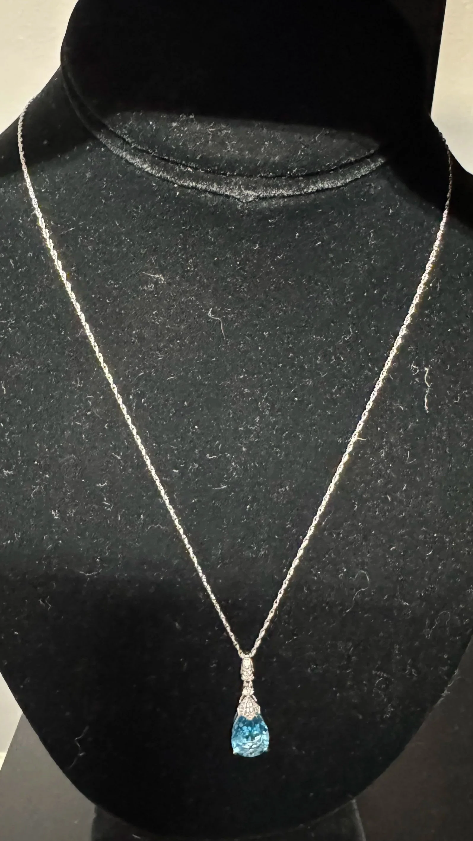 A shimmering blue gemstone pendant necklace displayed on a black fabric bust.