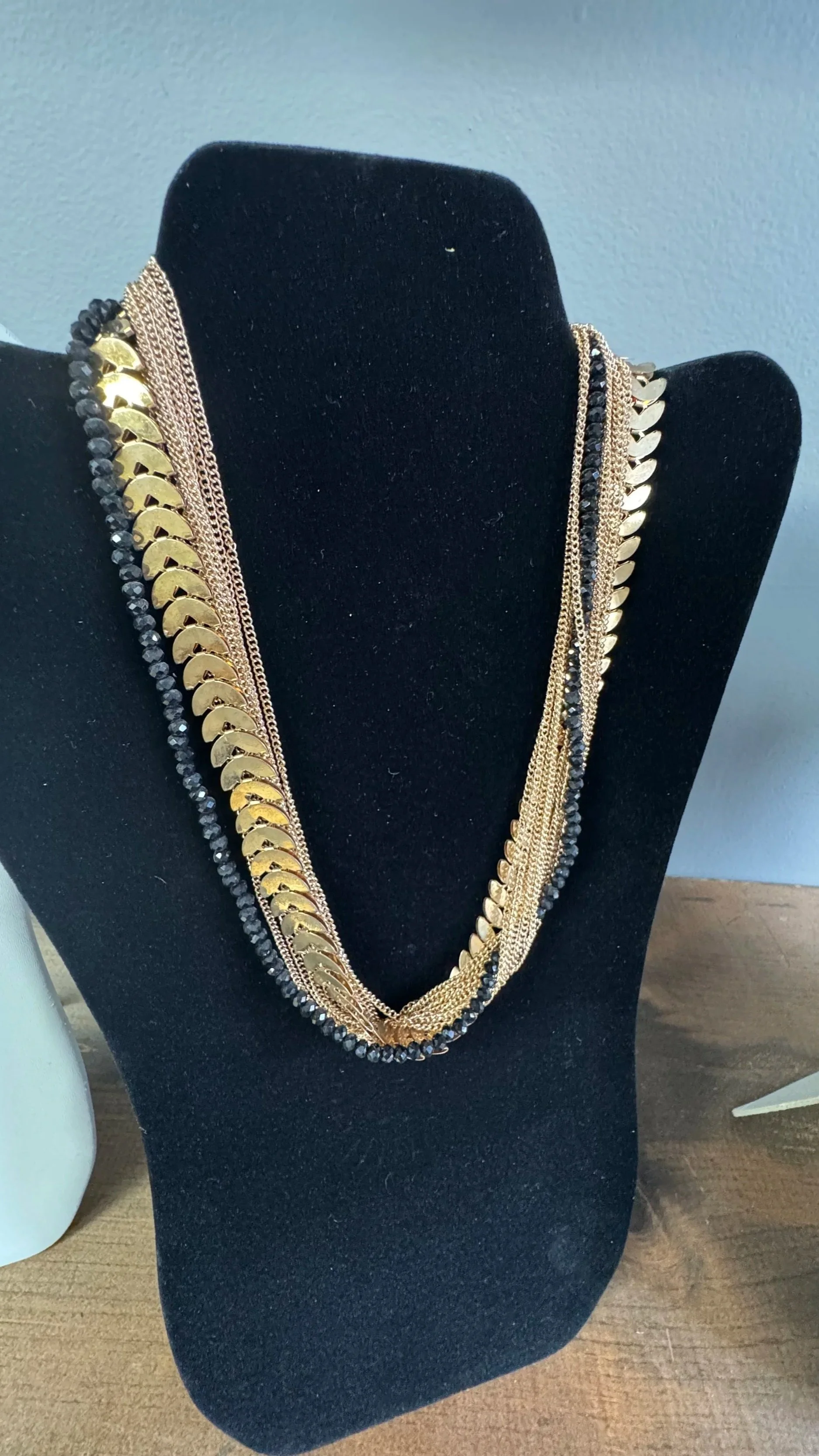 Multiple layered necklaces with gold and black beads displayed on a black jewelry stand.
