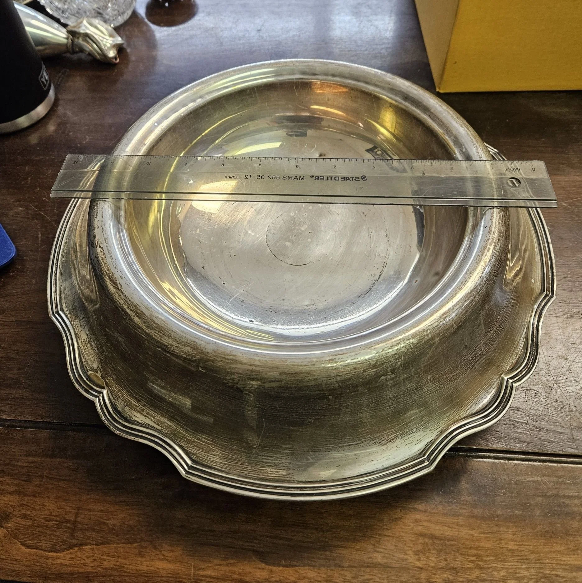A silver serving tray with a raised edge, placed on a wooden surface, with a clear ruler on top for measuring.