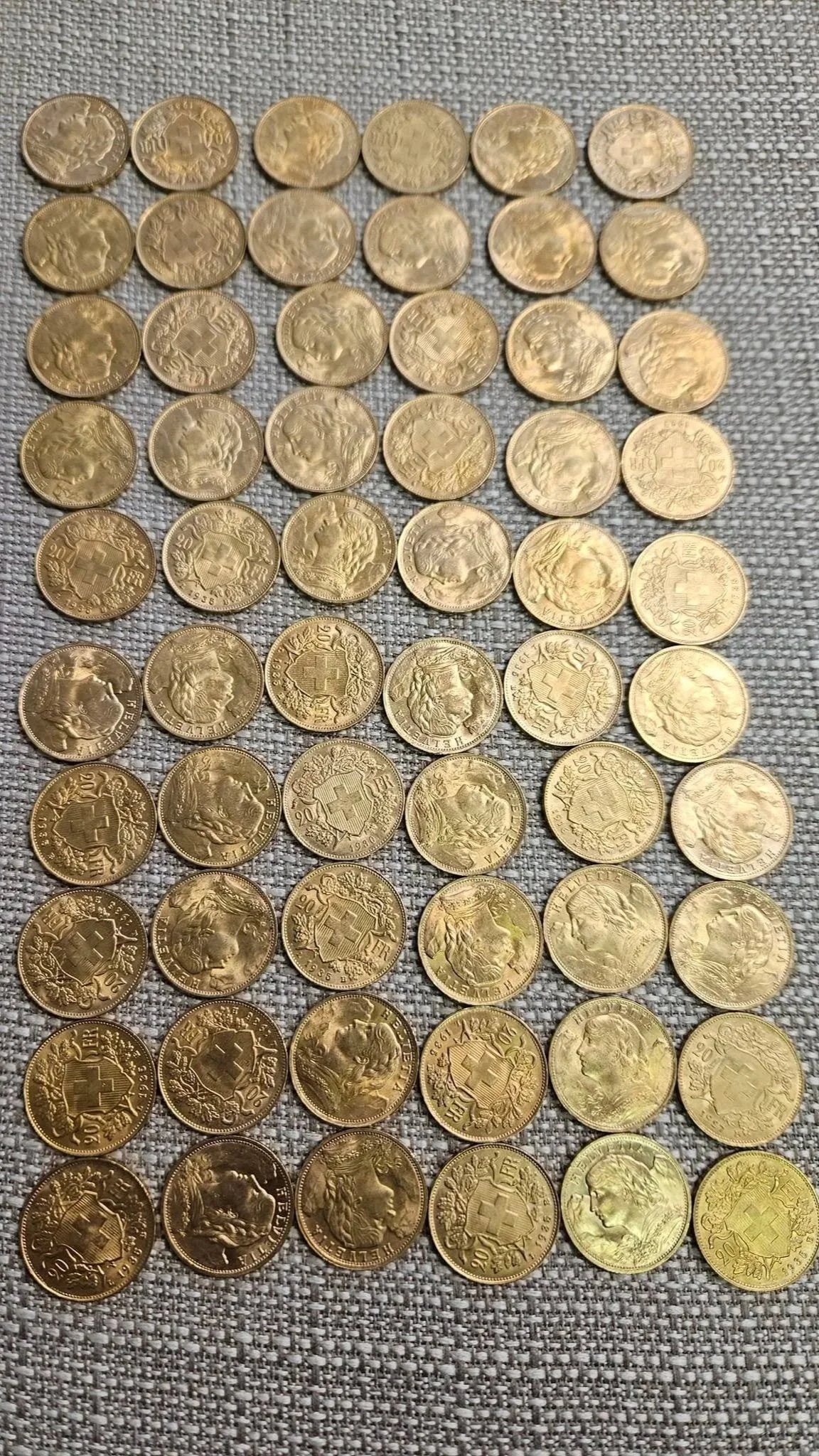 Collection of Swiss 20 franc gold coins with various portraits and designs, laid out on a textured grey surface.