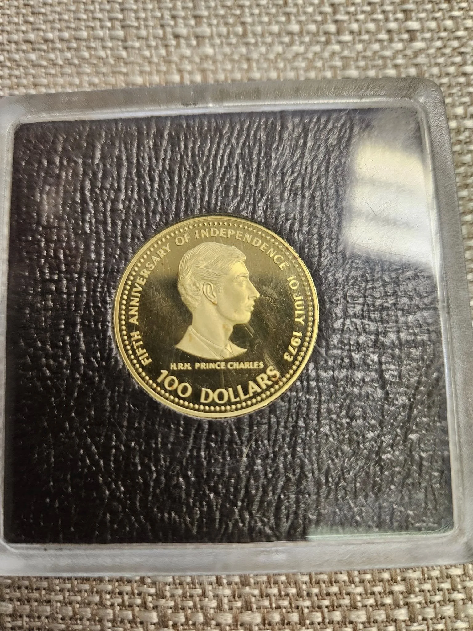 Gold-colored coin commemorating the 50th anniversary of independence, featuring a profile of Prince Charles with the inscription "H.R.H. Prince Charles" and the denomination "100 Dollars".