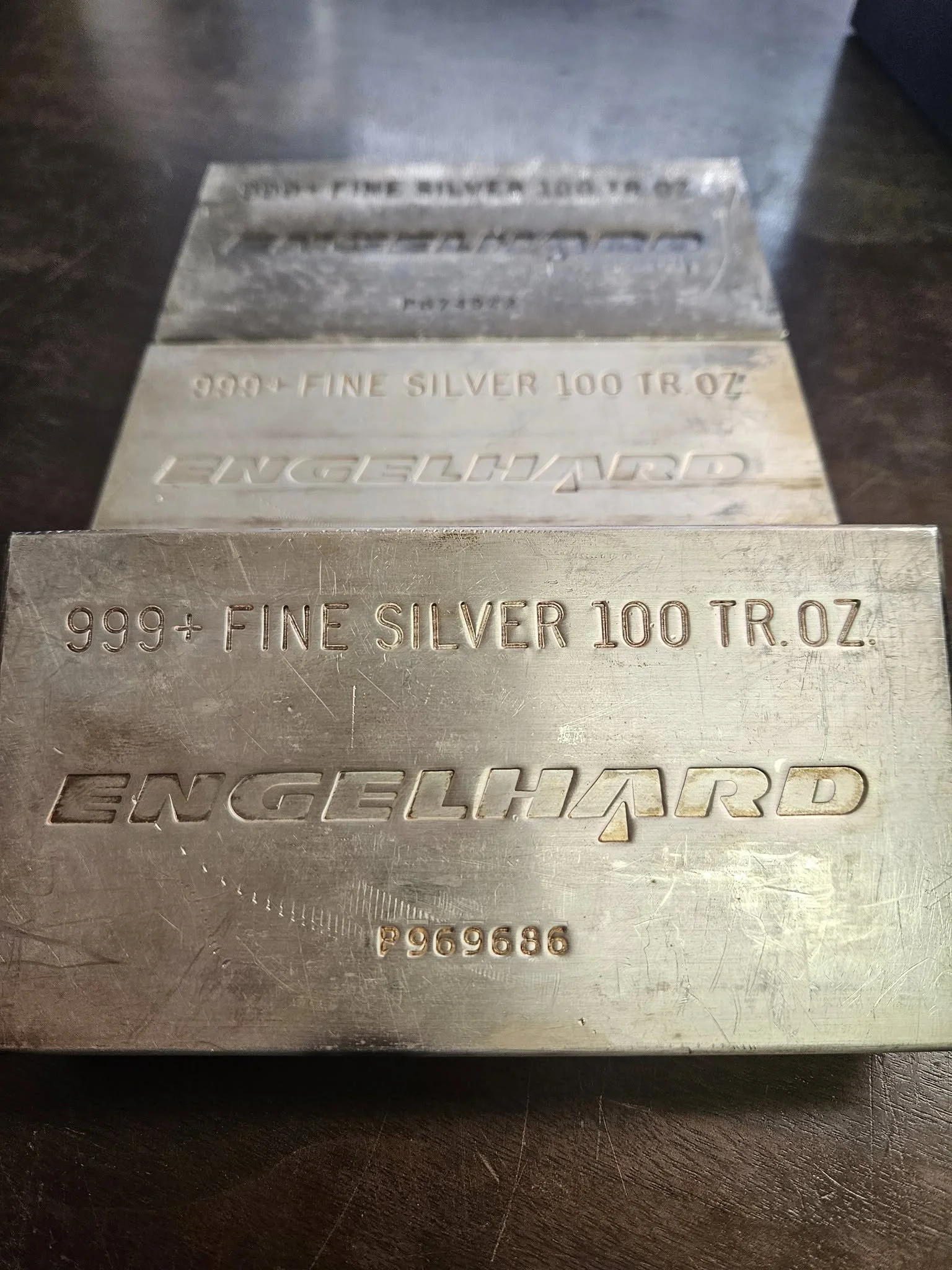 Close-up of metal ingots stamped with information about 999+ fine silver, 100 troy ounces, with the brand name Engelhart and a serial number.
