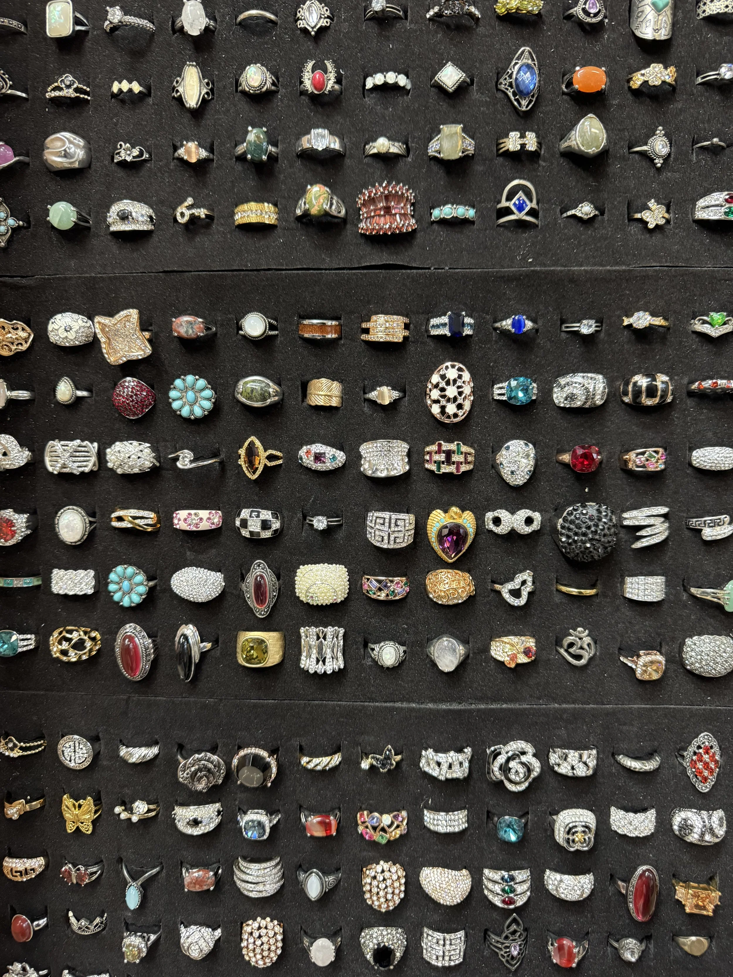 A display of multiple rows of various rings on a black surface, featuring different designs, colors, and styles.