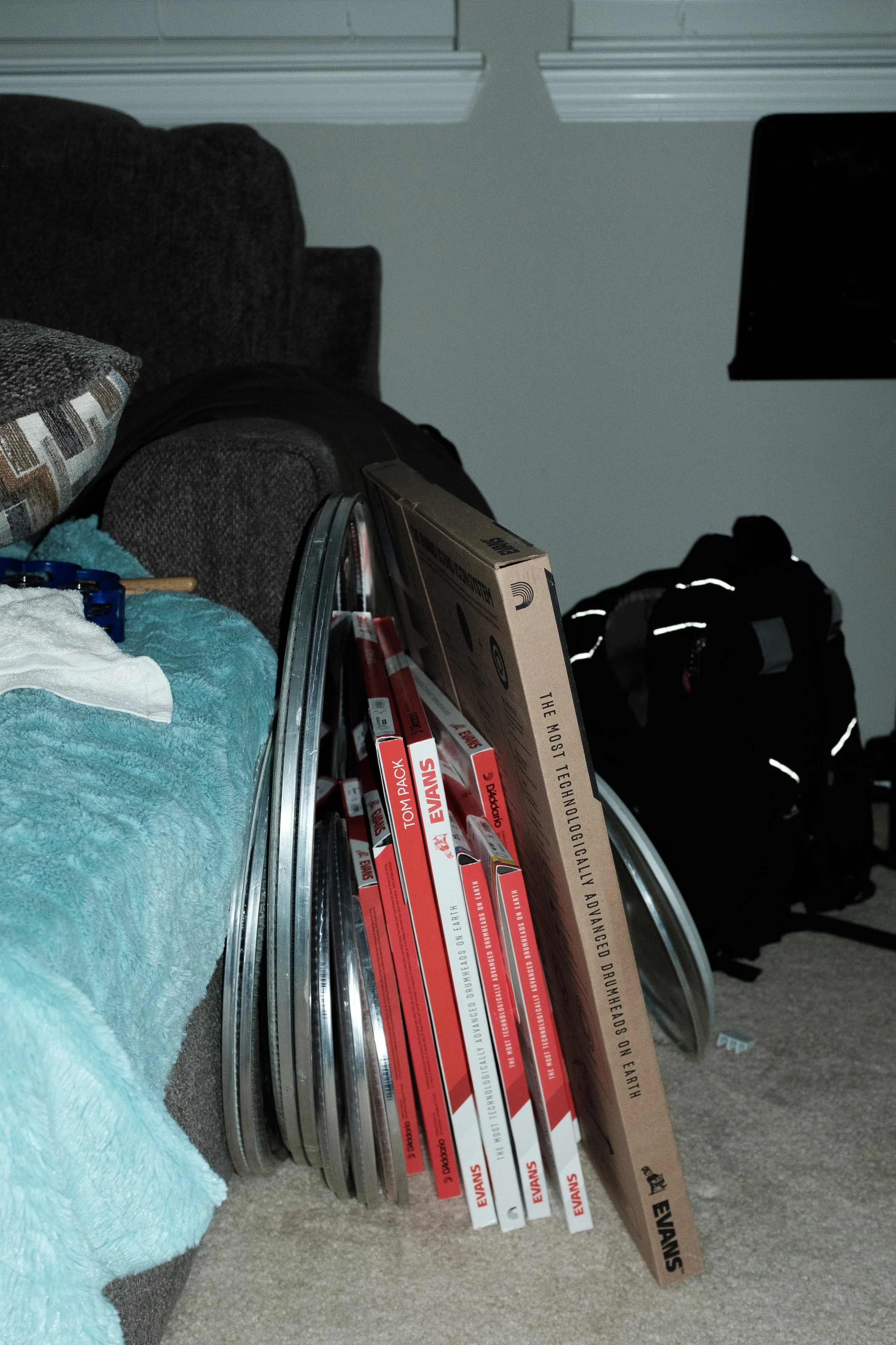 A pile of drum head boxes resting against a gray couch in a music studio.