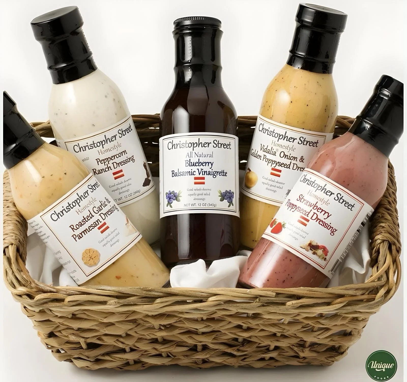 A woven basket filled with five bottles of salad dressings, each labeled with different flavors including blueberry balsamic vinaigrette, peppercorn ranch dressing, Vidalia onion & golden poppyseed dressing, roasted garlic & parmesan dressing, and strawberry poppyseed dressing.