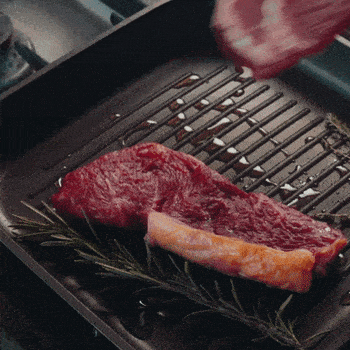 A piece of raw steak and a strip of bacon on a grill pan.