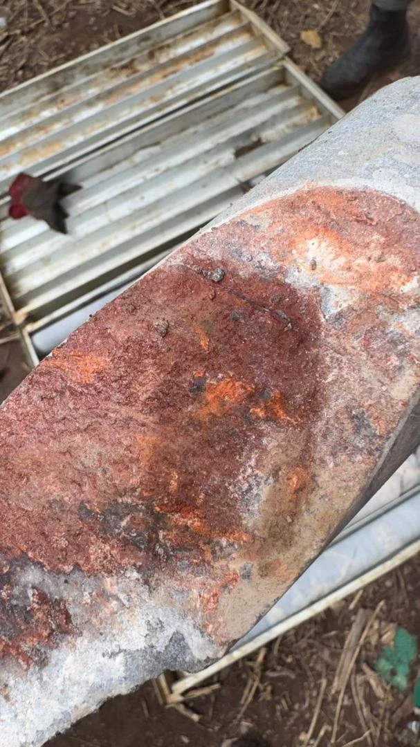 Rusty metal beam with a rough surface and some corrosion, in an outdoor construction area with a metal scaffolding in the background.