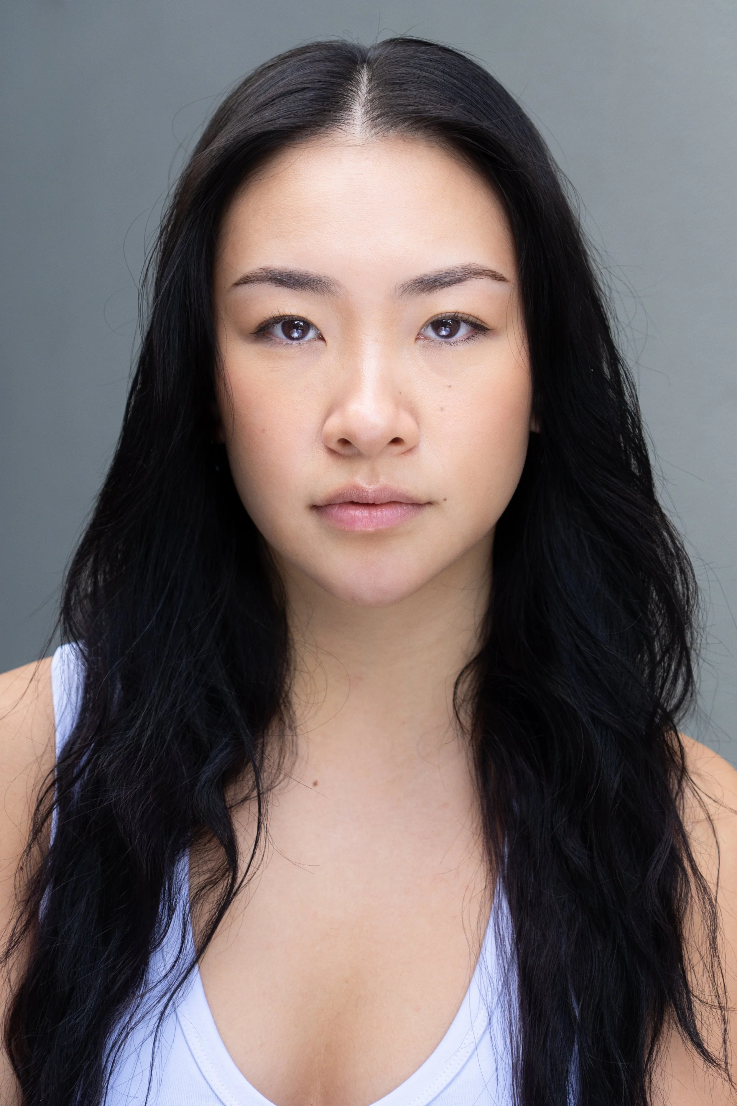 A young woman with long, wavy black hair wearing a white top.