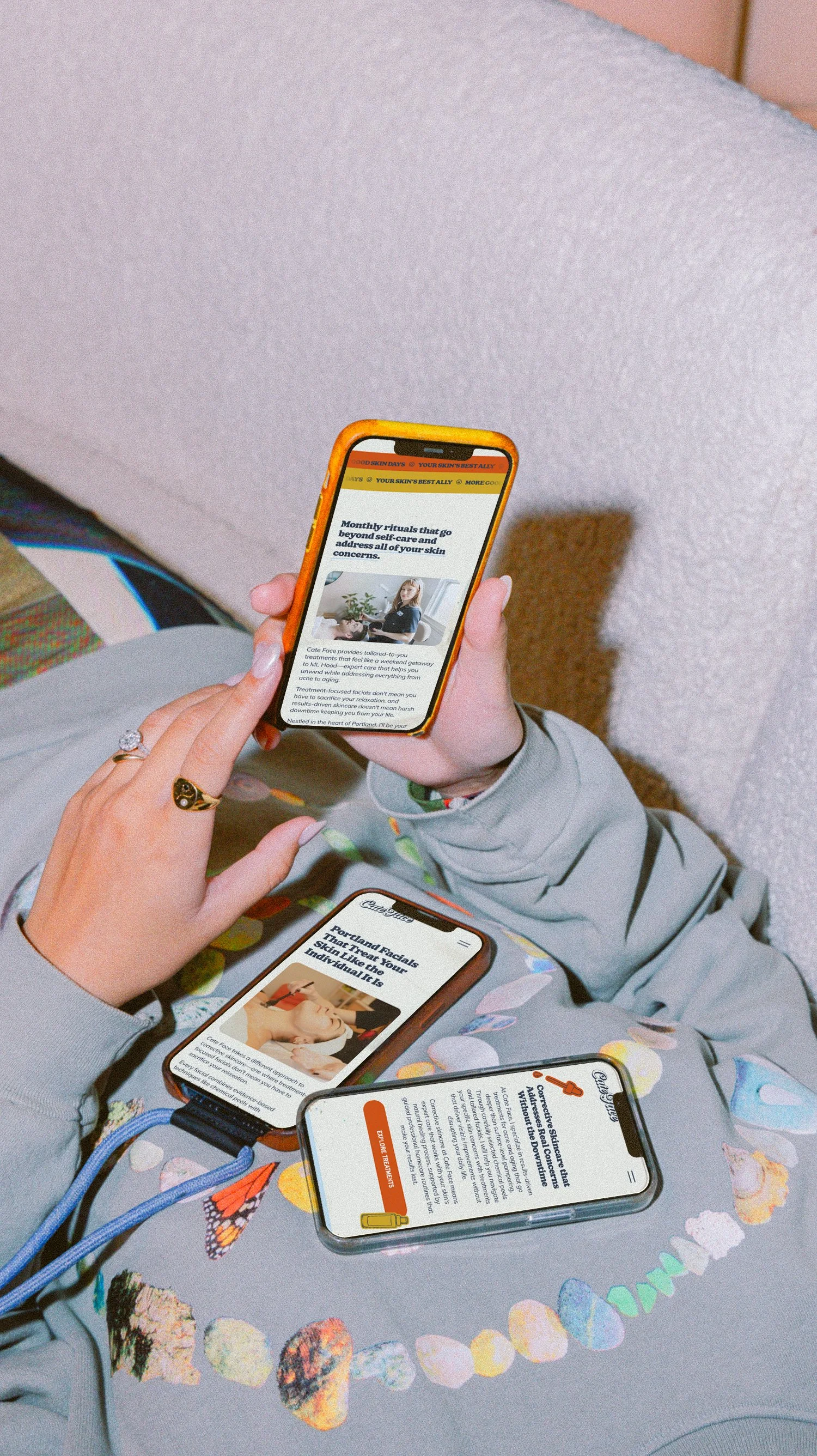 Three people holding smartphones displaying skincare article webpages, sitting on a colorful butterfly-patterned blanket.Multiple smartphones with skincare website pages, designed by Marmalade Creative Studio, on someone's lap, wearing a gray hoodie