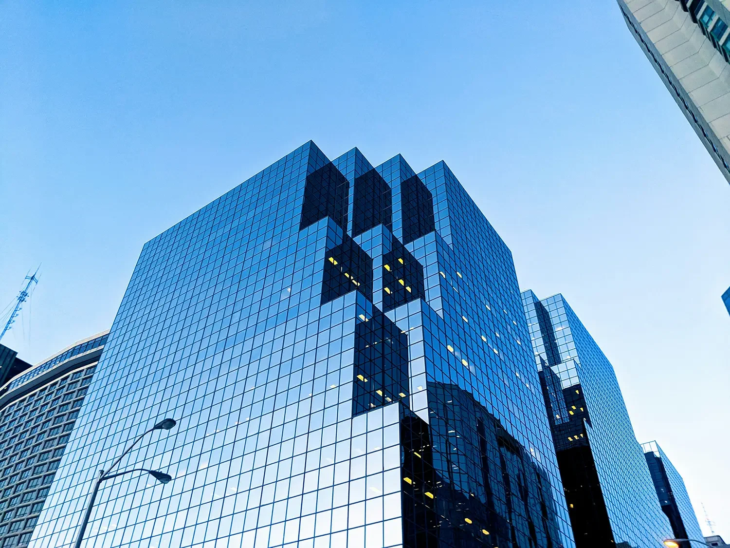 Tall modern glass office building with a reflective blue surface, set against a clear blue sky.