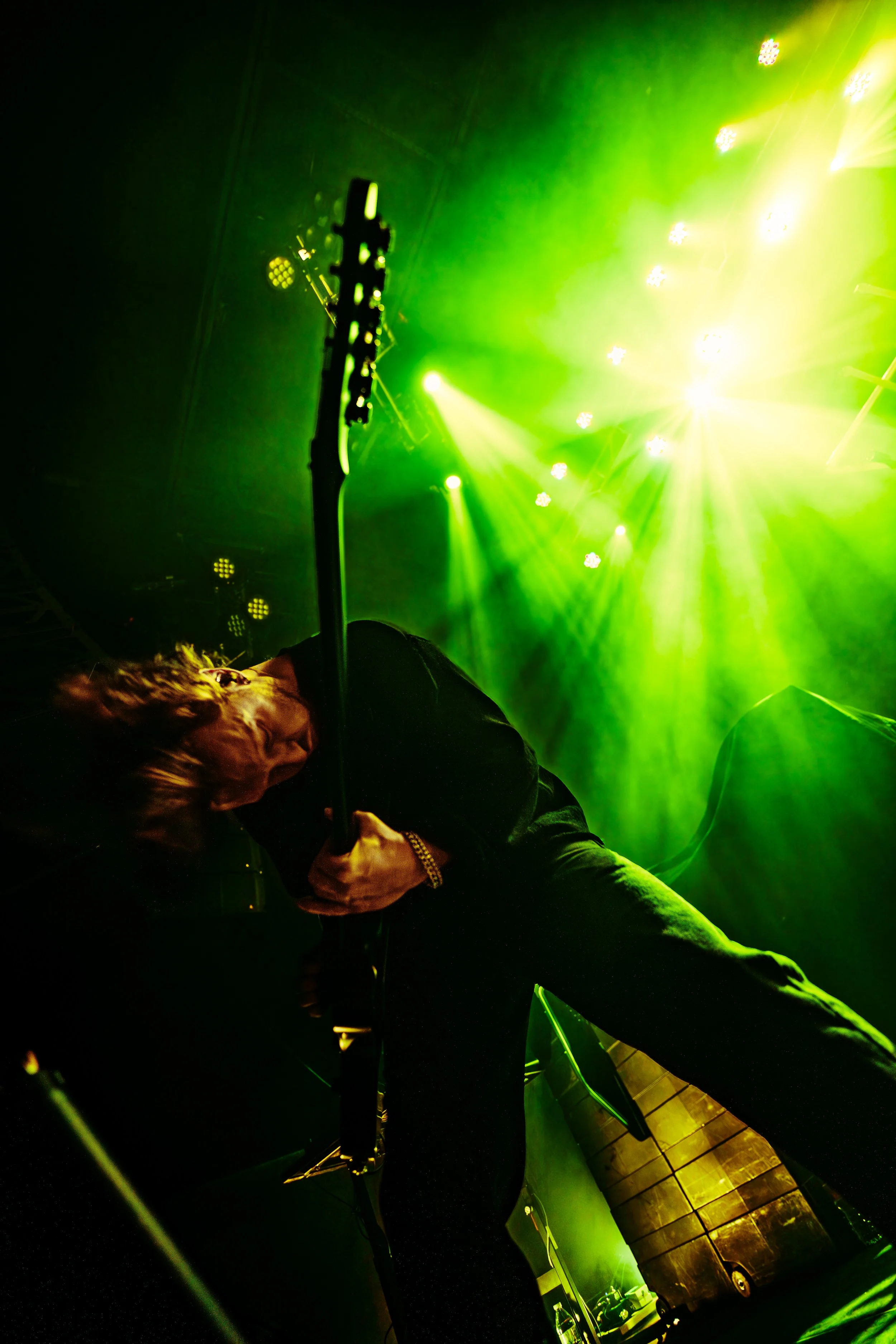 A musician playing an electric guitar on stage with green and yellow stage lights.