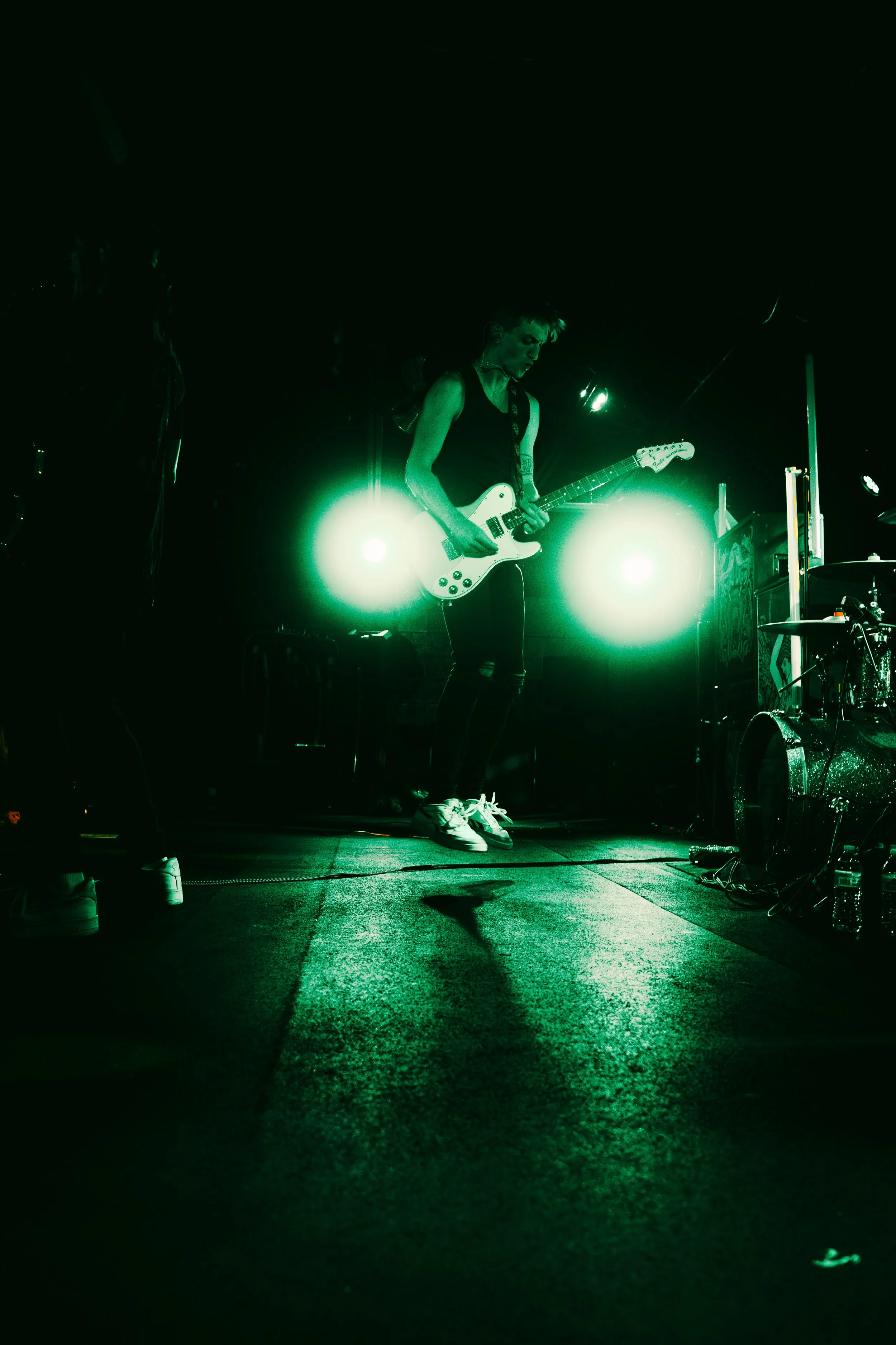 A woman playing electric guitar on stage with green stage lights illuminating her.
