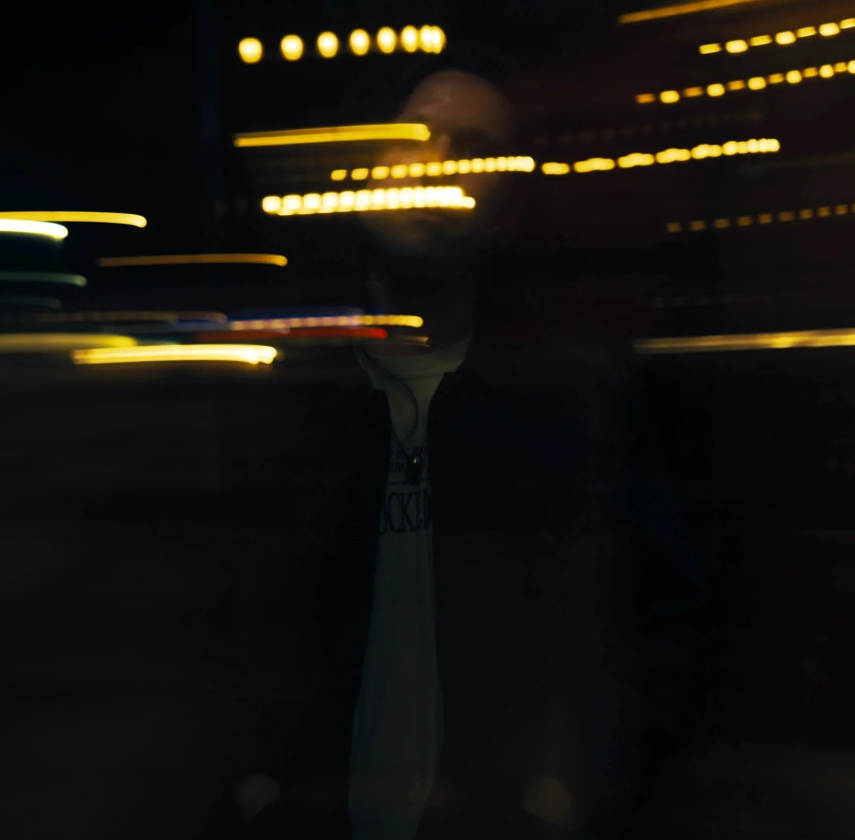 Blurred nighttime image of a person with city lights streaking behind them, reflecting in a window.