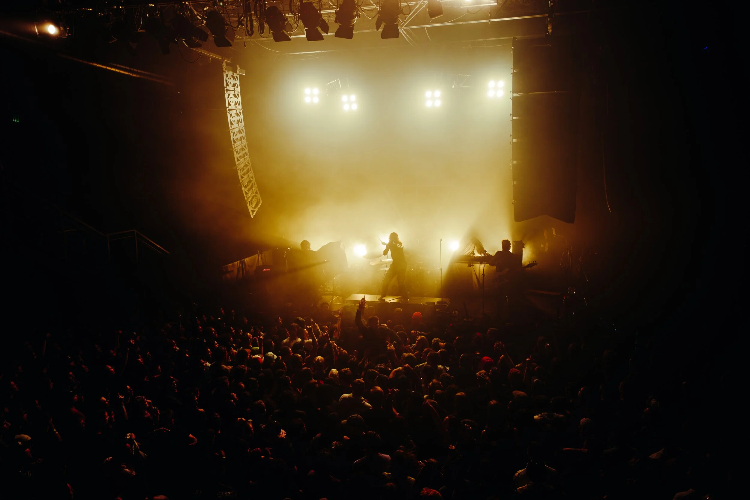 Stage with bright yellow lights, musicians performing, and a large audience watching at a concert or music event.