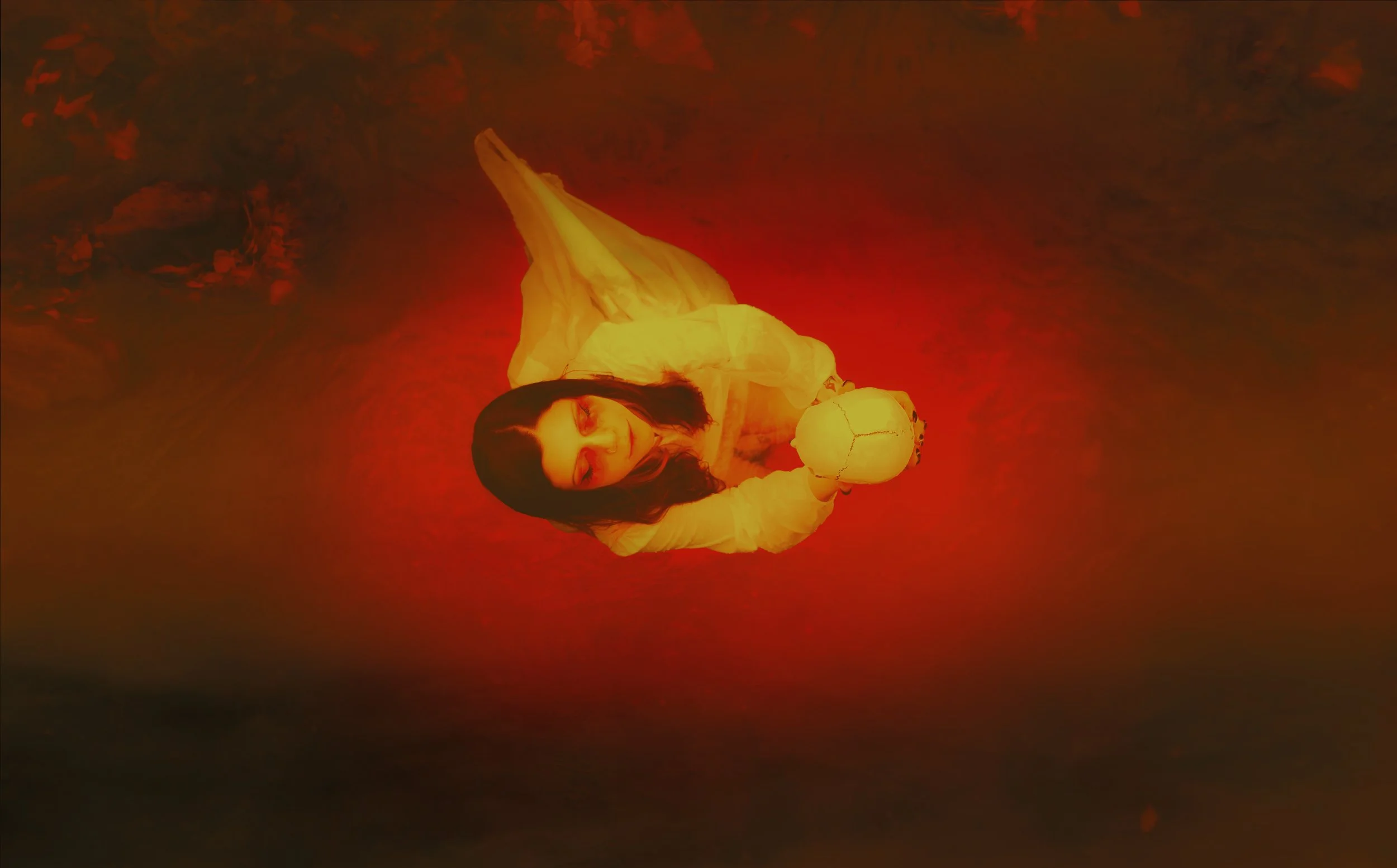 A woman dressed in a flowing yellow dress, holding a pumpkin, standing in a shallow body of water with a reddish glow, creating a surreal, atmospheric scene.